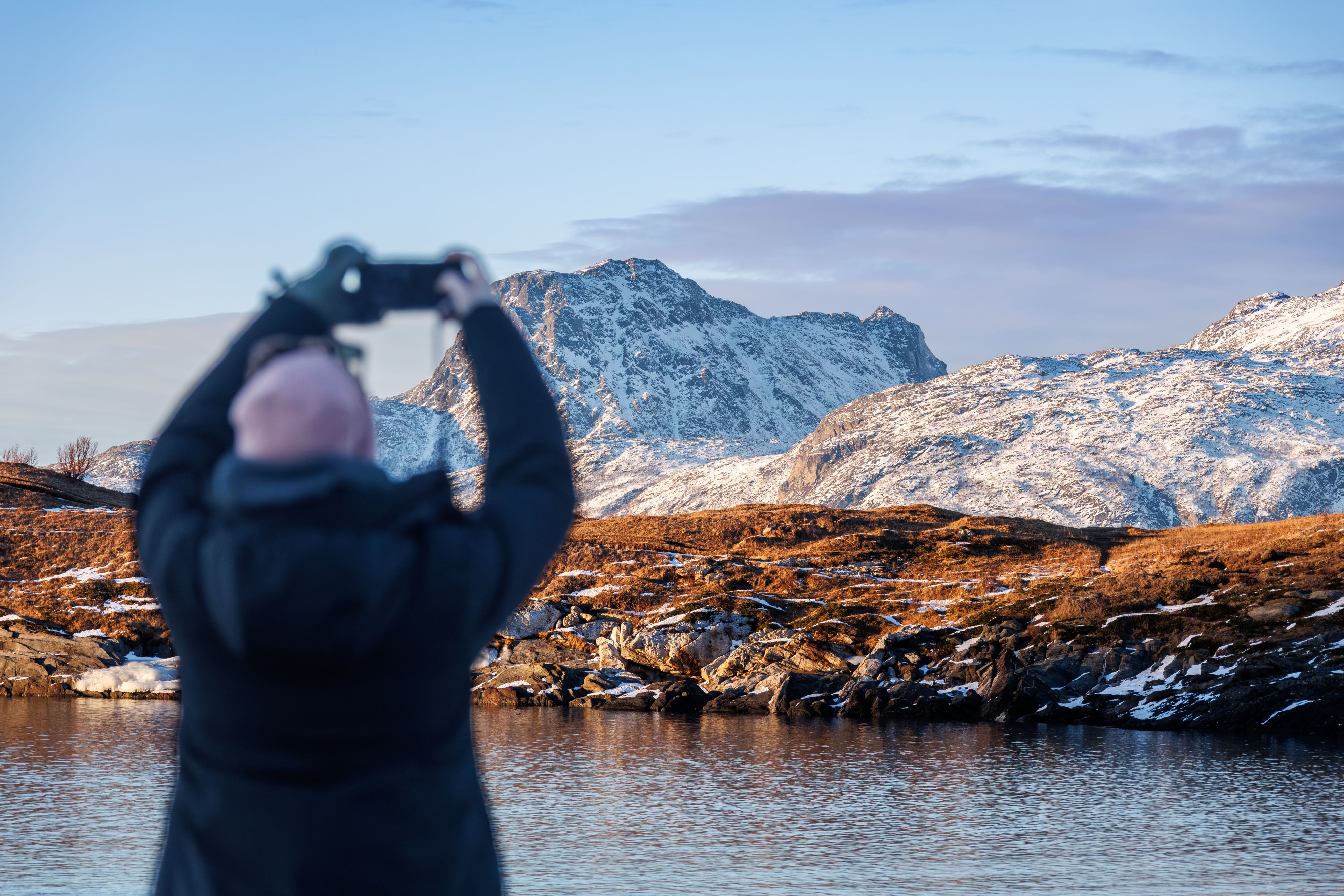 Besøkende som tar et bilde av snødekte fjell ved en stille innsjø på en arktisk kystvandring i Norge