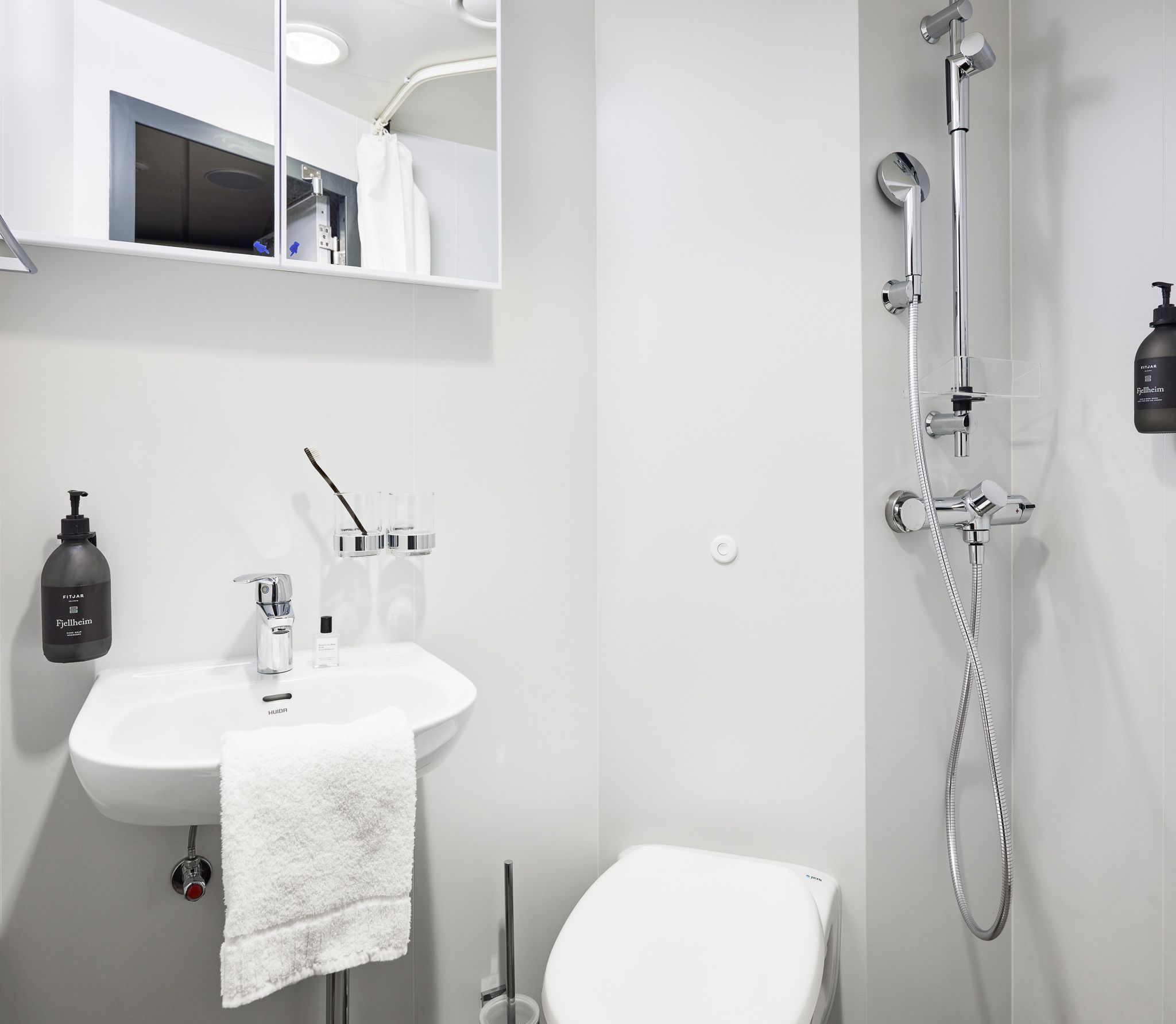 Modernes Kreuzfahrtkabinen-Badezimmer mit Dusche, Toilette, Waschbecken, Spiegelschrank, frischen Handtüchern und kostenlosen Pflegeprodukten.