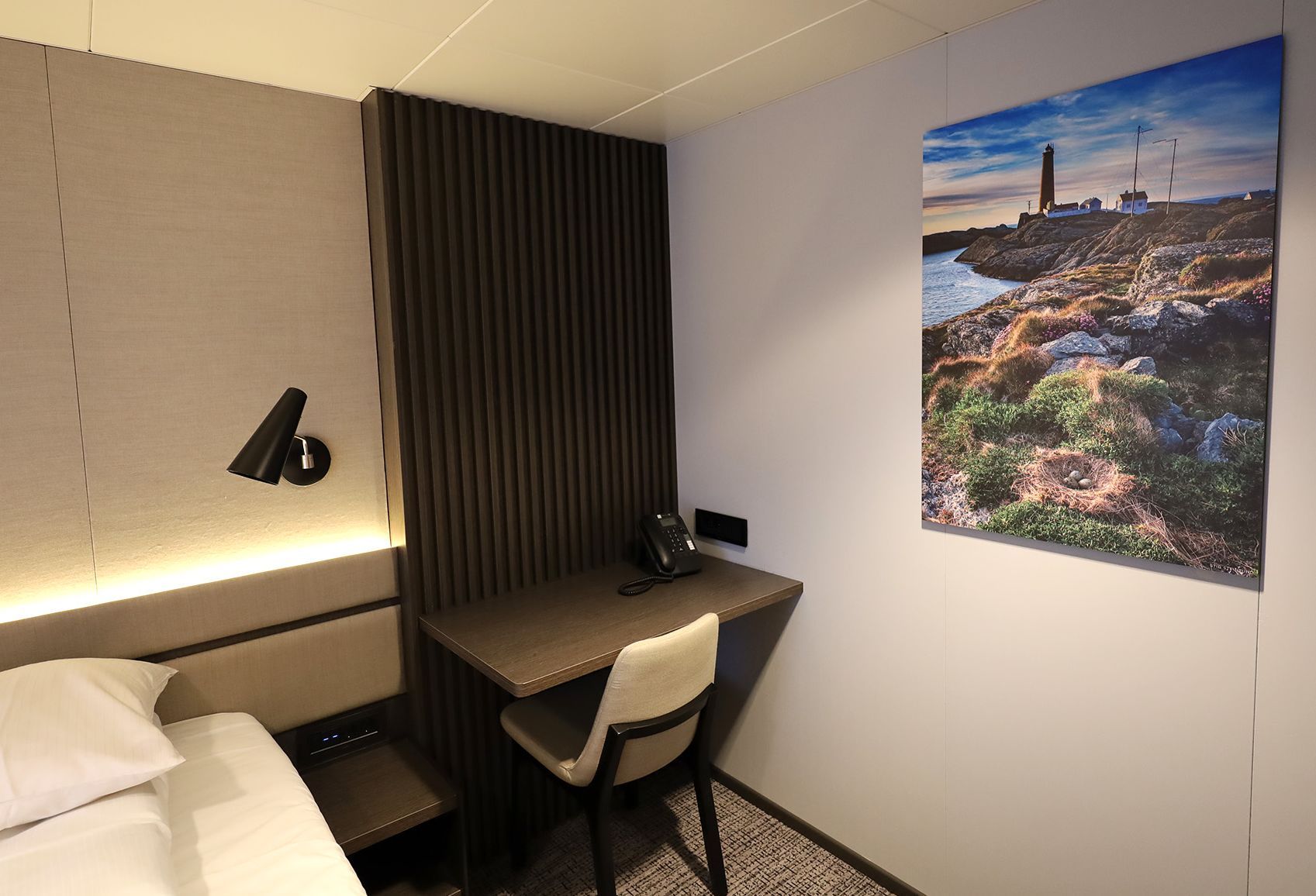 Suite-Arbeitsbereich mit integriertem Schreibtisch, Stuhl, Telefon, Beleuchtung am Bett und gerahmten Kunstwerken in einem modernen, minimalistischen Design.