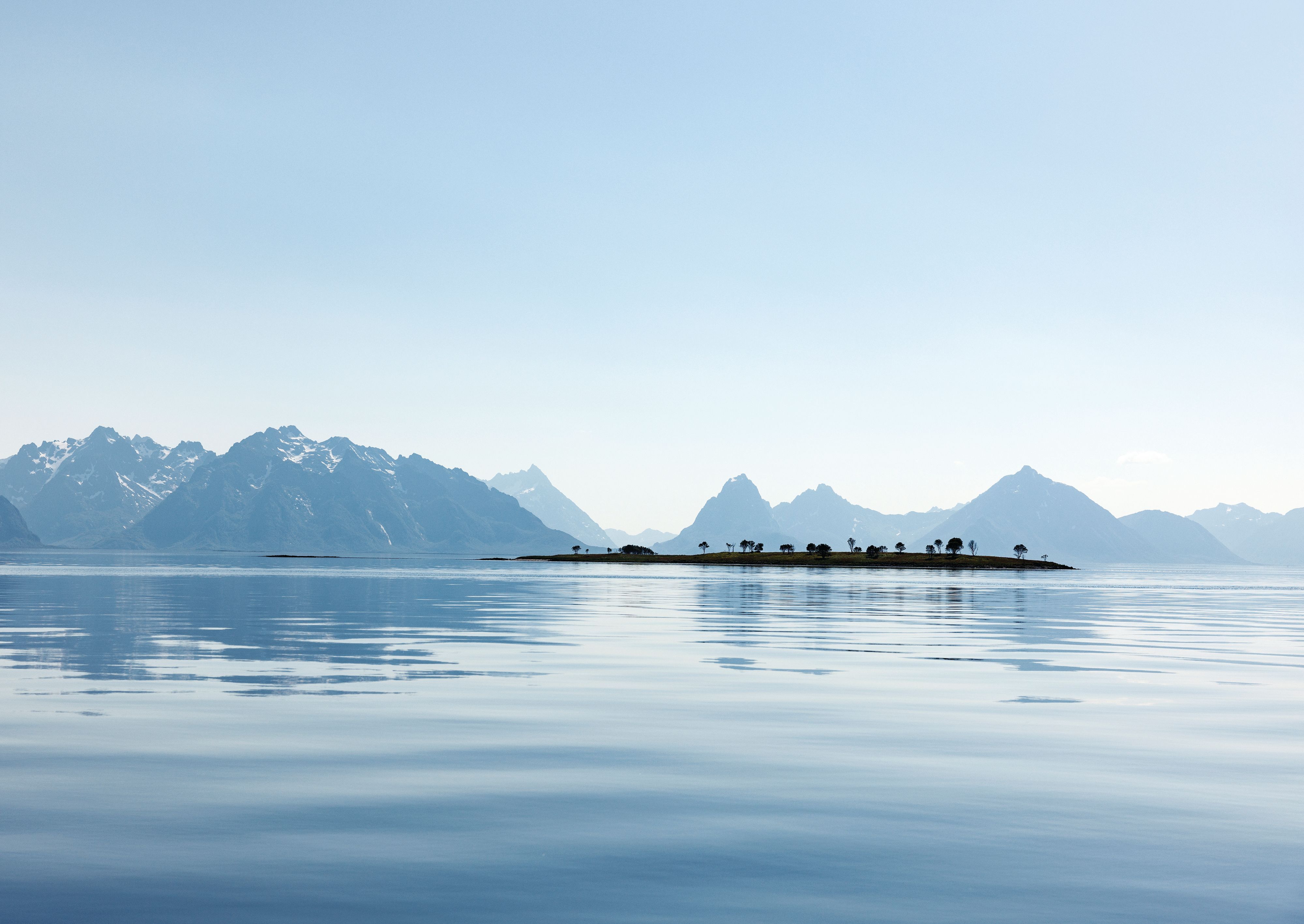 Calm Arctic waters with a small island and snow-capped mountains along the Norwegian coast.