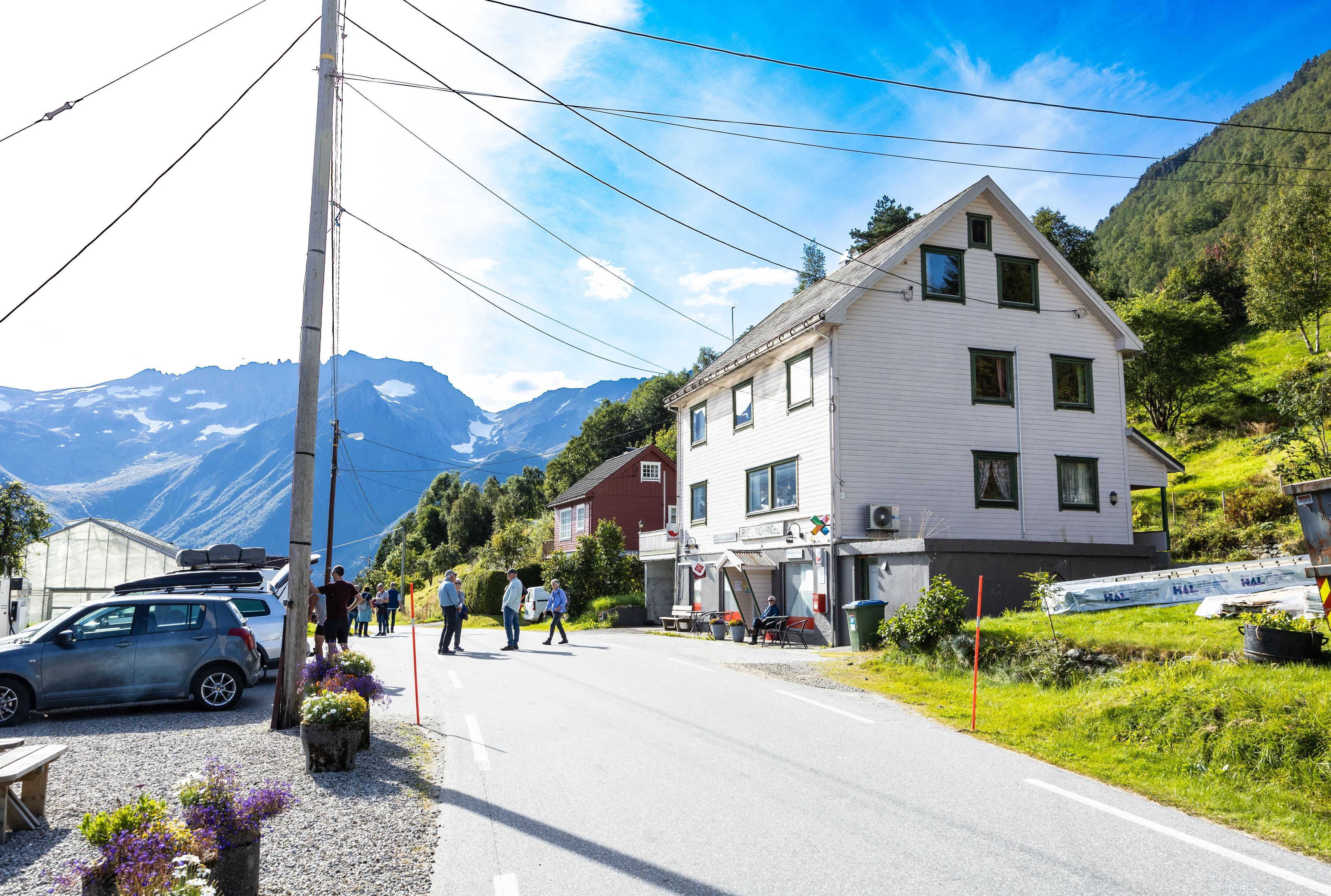 Visitors at a traditional village shop and white wooden house below snowy mountains in rural Norway