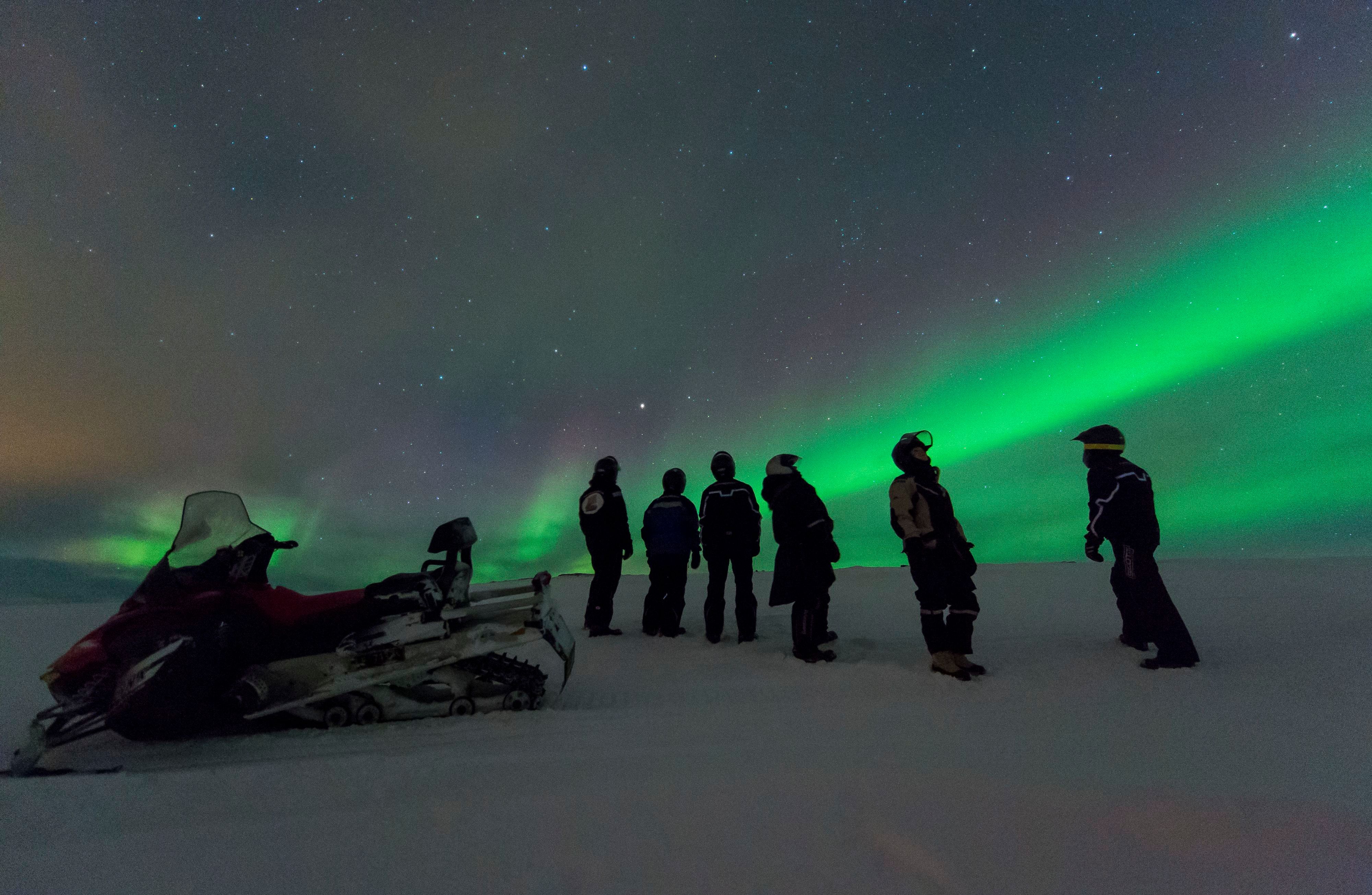 Guests watching the Northern Lights beside snowmobiles on a night tour from Kjøllefjord.