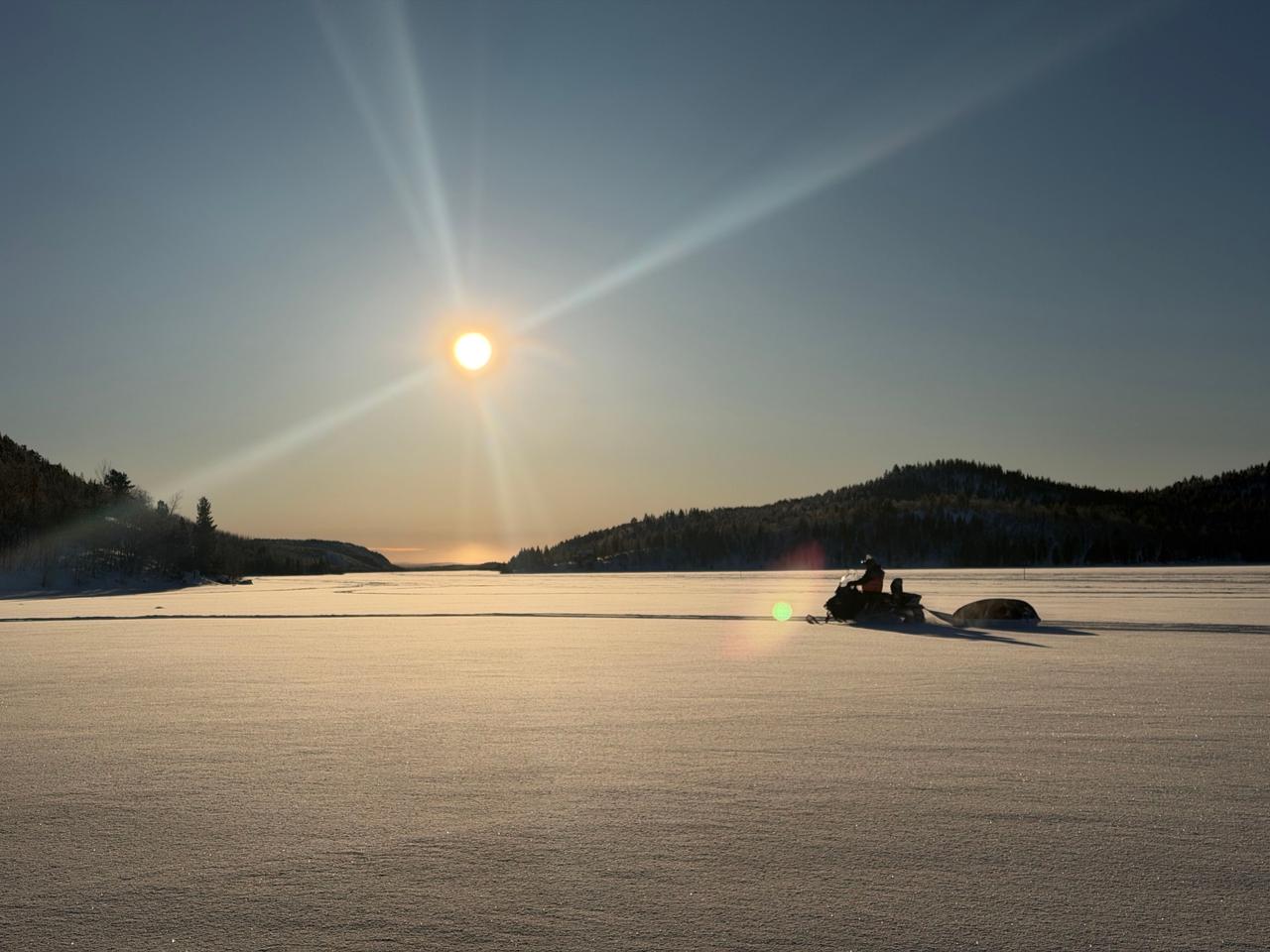 Silhouette of a snowmobile crossing a frozen lake under a low winter sun on a snowmobile safari in Kirkenes, Norway