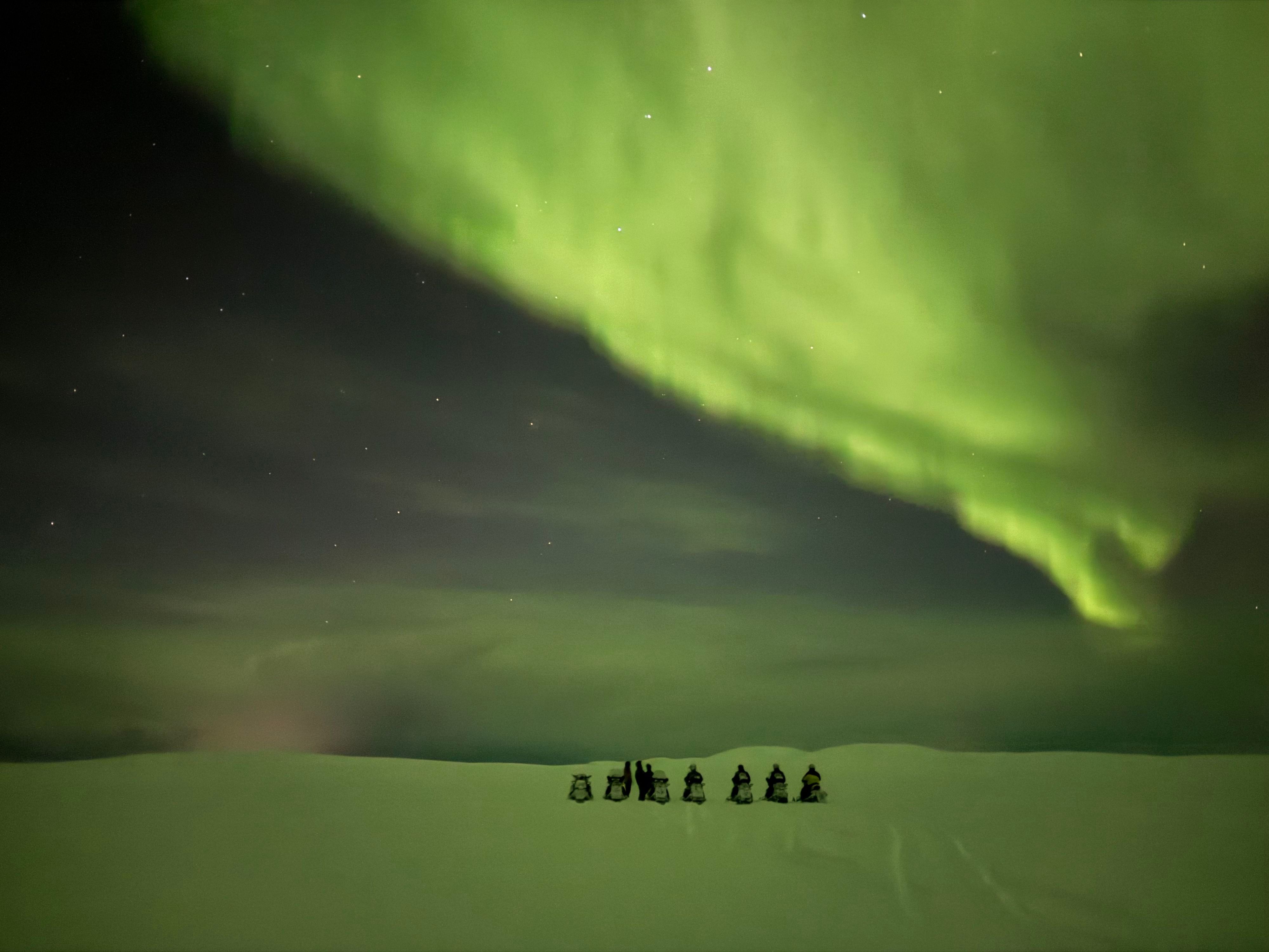 Snowmobiles parked beneath the Aurora Borealis during a night tour from Kjøllefjord.