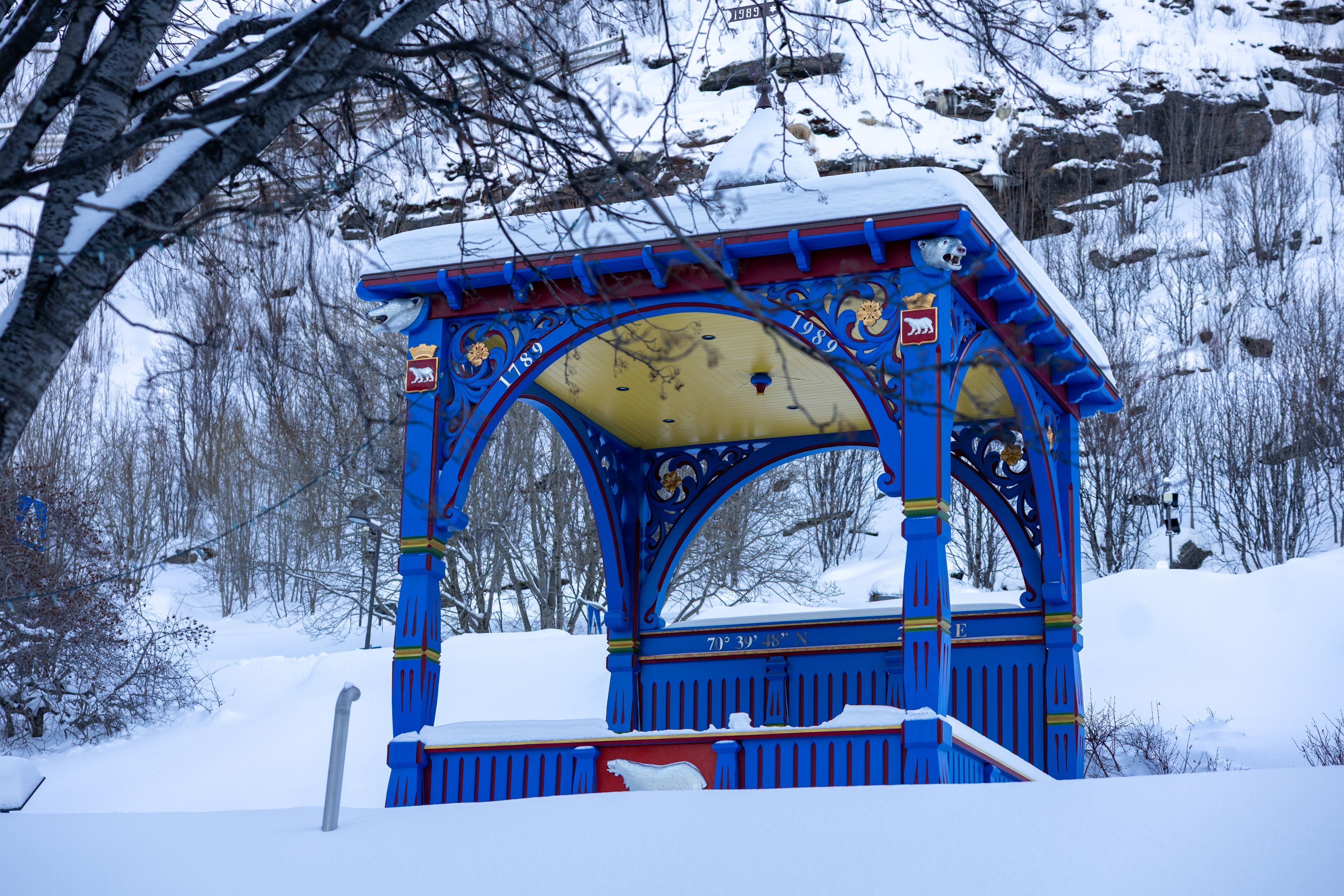 Utsmykket blått og gult paviljongbygg med isbjørnemblemer omgitt av snø på en vinterlig byvandring i Hammerfest, Norge