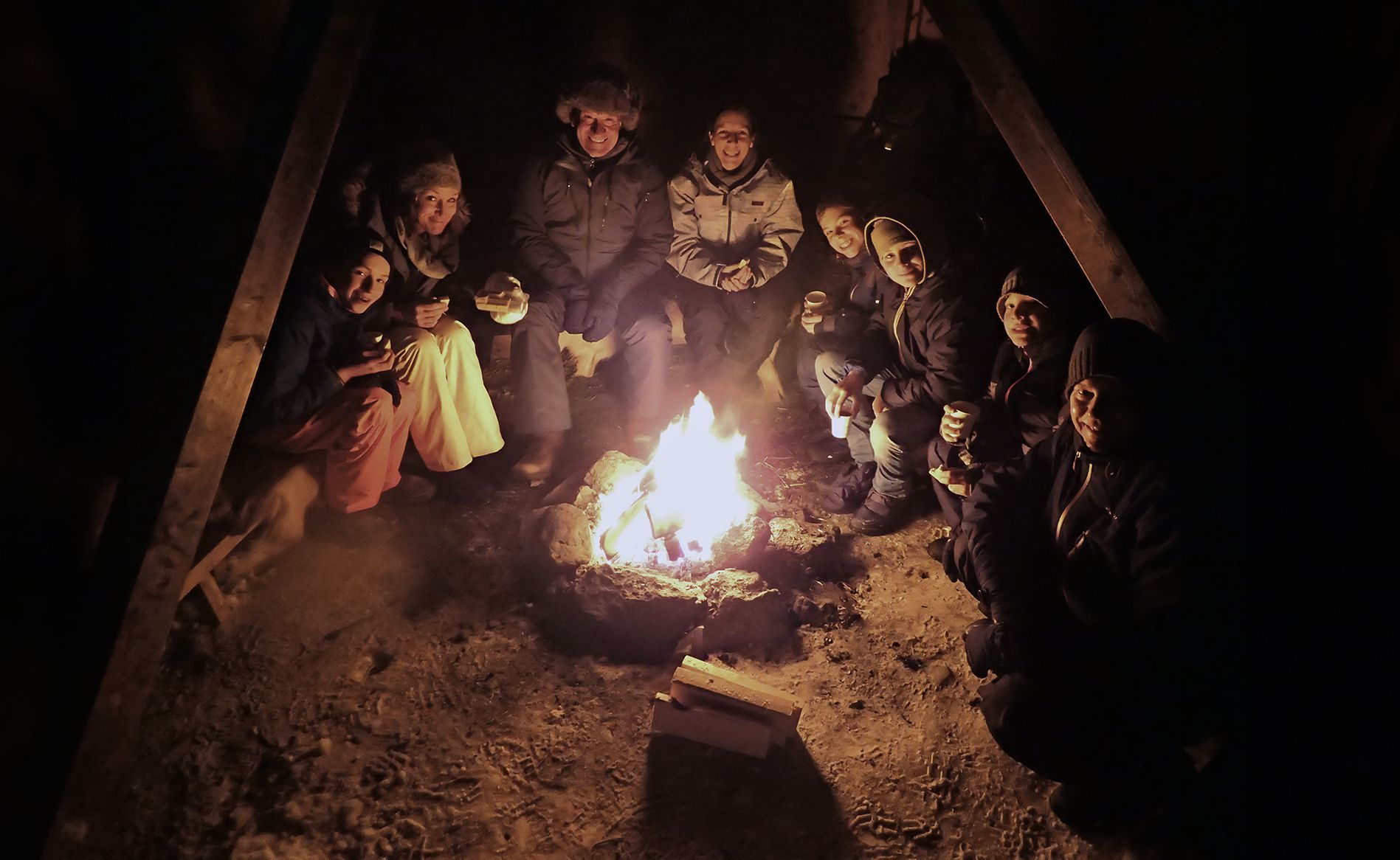 Nach einer geführten Schneeschuhwanderung in der Nähe von Tromsø versammelten sich die Gäste um ein knisterndes Lagerfeuer in einer traditionellen arktischen Hütte, genossen warme Getränke und gemeinsam einen gemütlichen Winterabend.