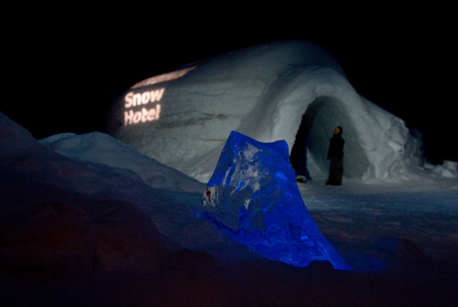Den opplyste inngangen til Snowhotel Kirkenes om natten, omgitt av snø- og isskulpturer.