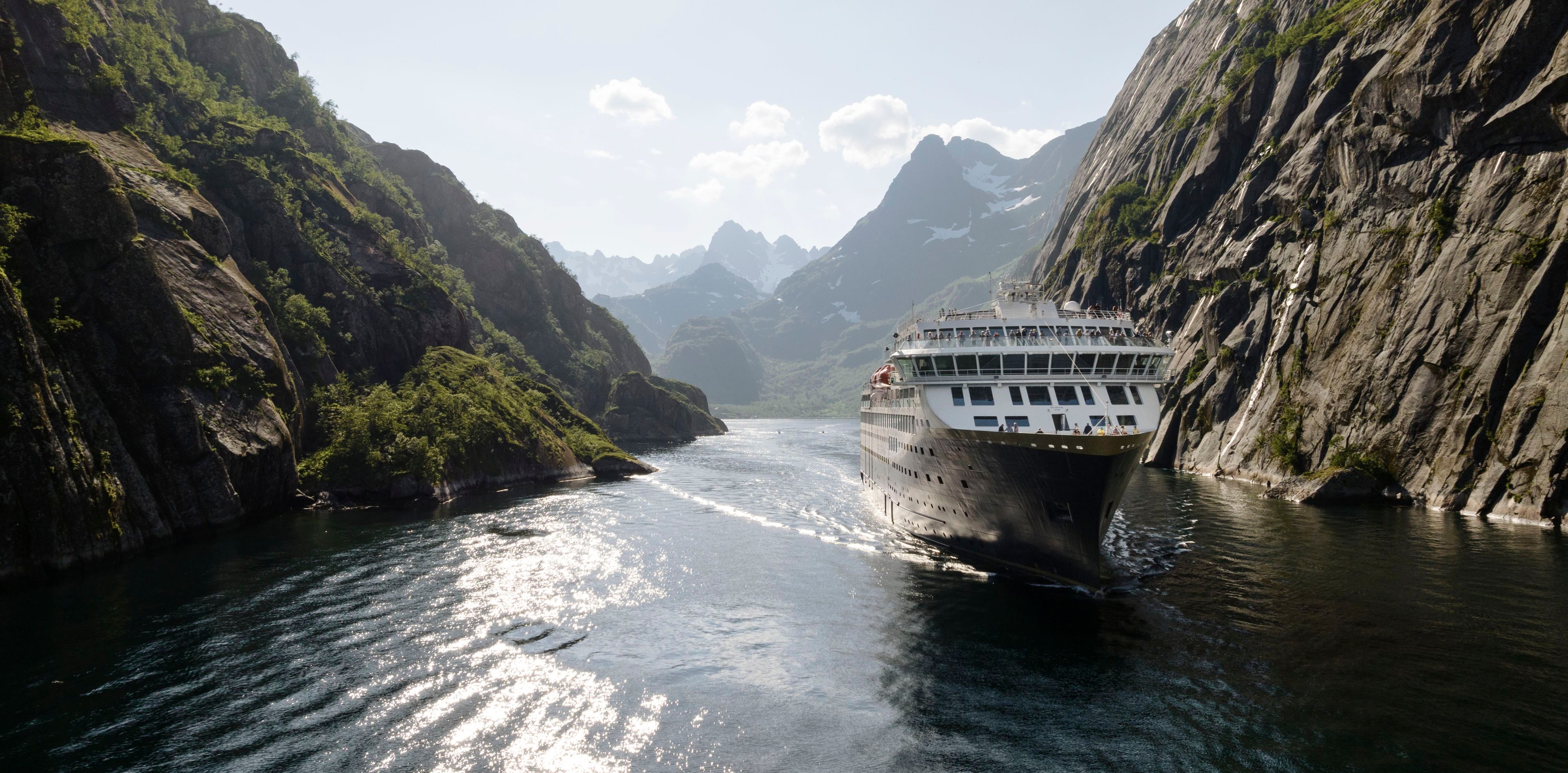 Havila Kystruten-skip som seiler gjennom en smal norsk fjord omgitt av bratte fjell.
