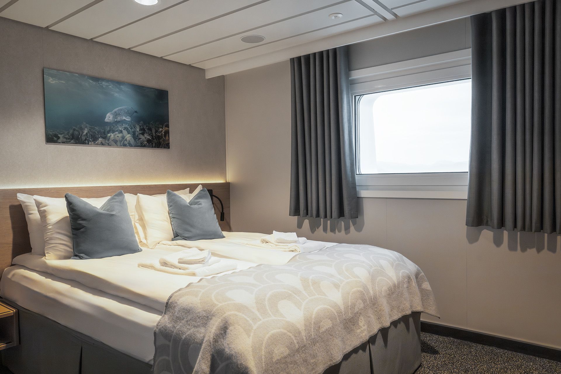 Schlafzimmer der Aft View Mini Suite mit einem Kingsize-Bett mit hochwertiger Bettwäsche, Leselampen und einem großen Fenster mit Meerblick nach achtern.