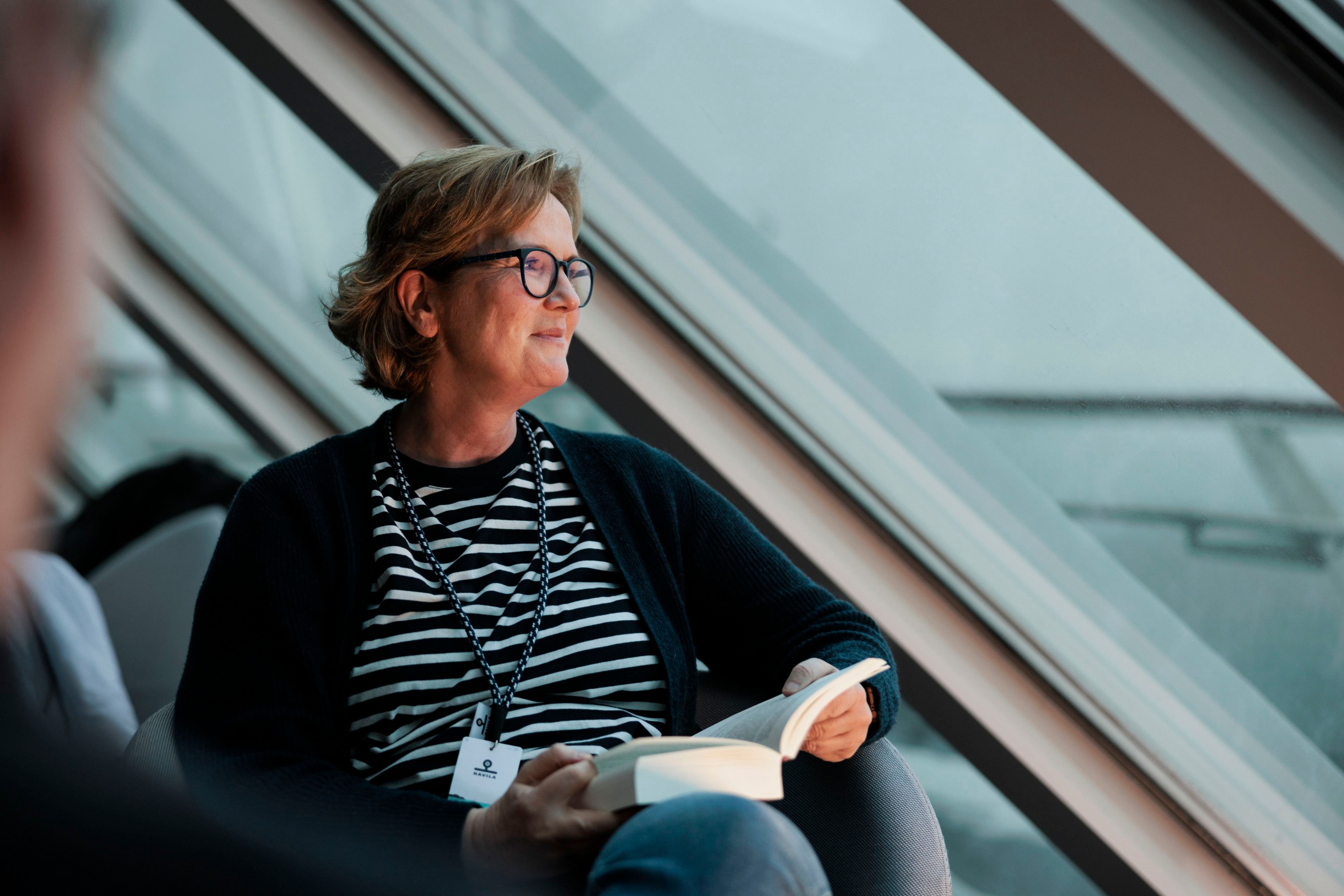Guest relaxing with a book in Havila Voyages' panoramic lounge while enjoying the coastal views.