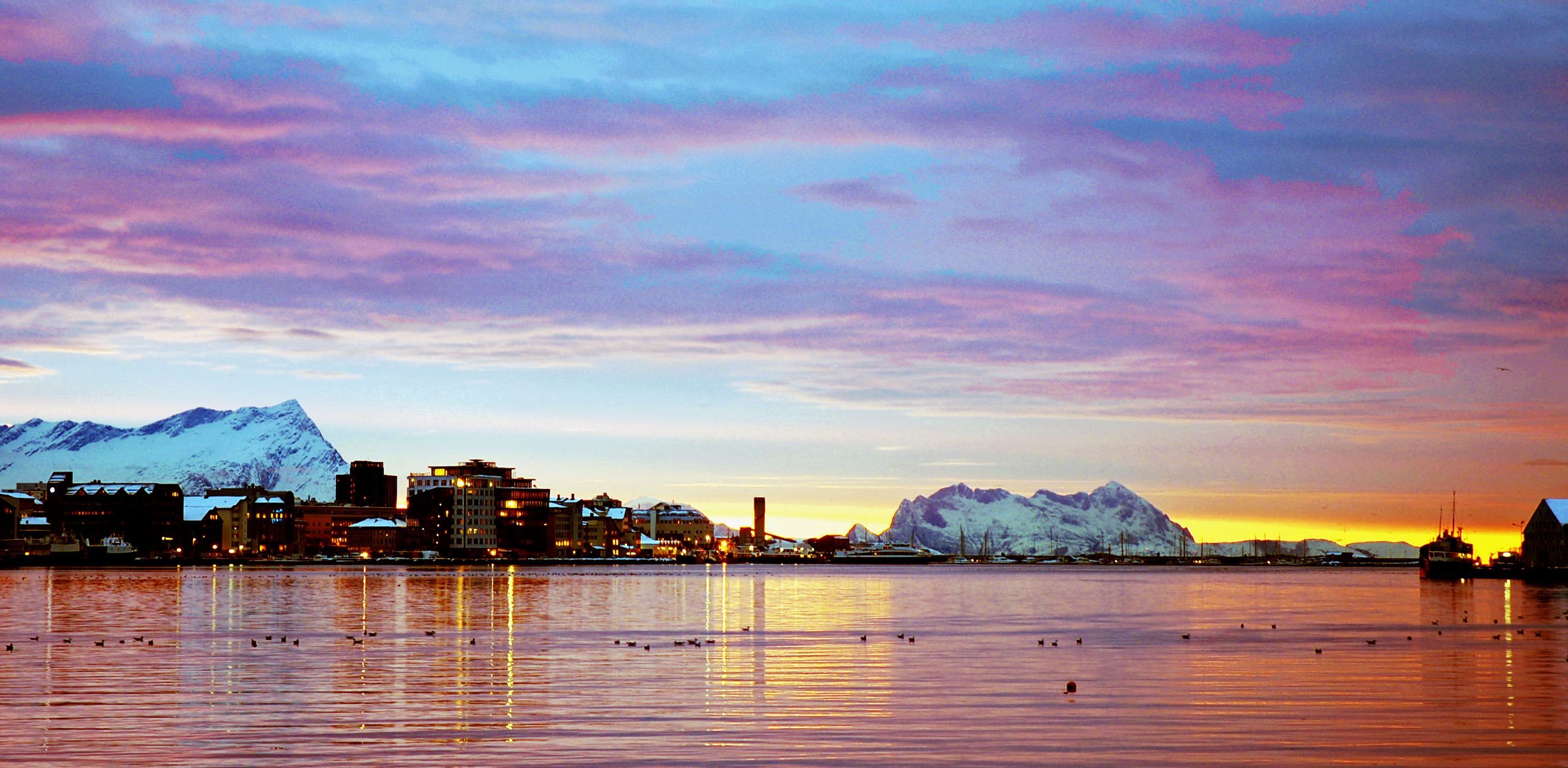 Bodøs Uferpromenade bei Sonnenuntergang mit schneebedeckten Bergen und rosafarbenem und goldenem Licht auf dem Wasser