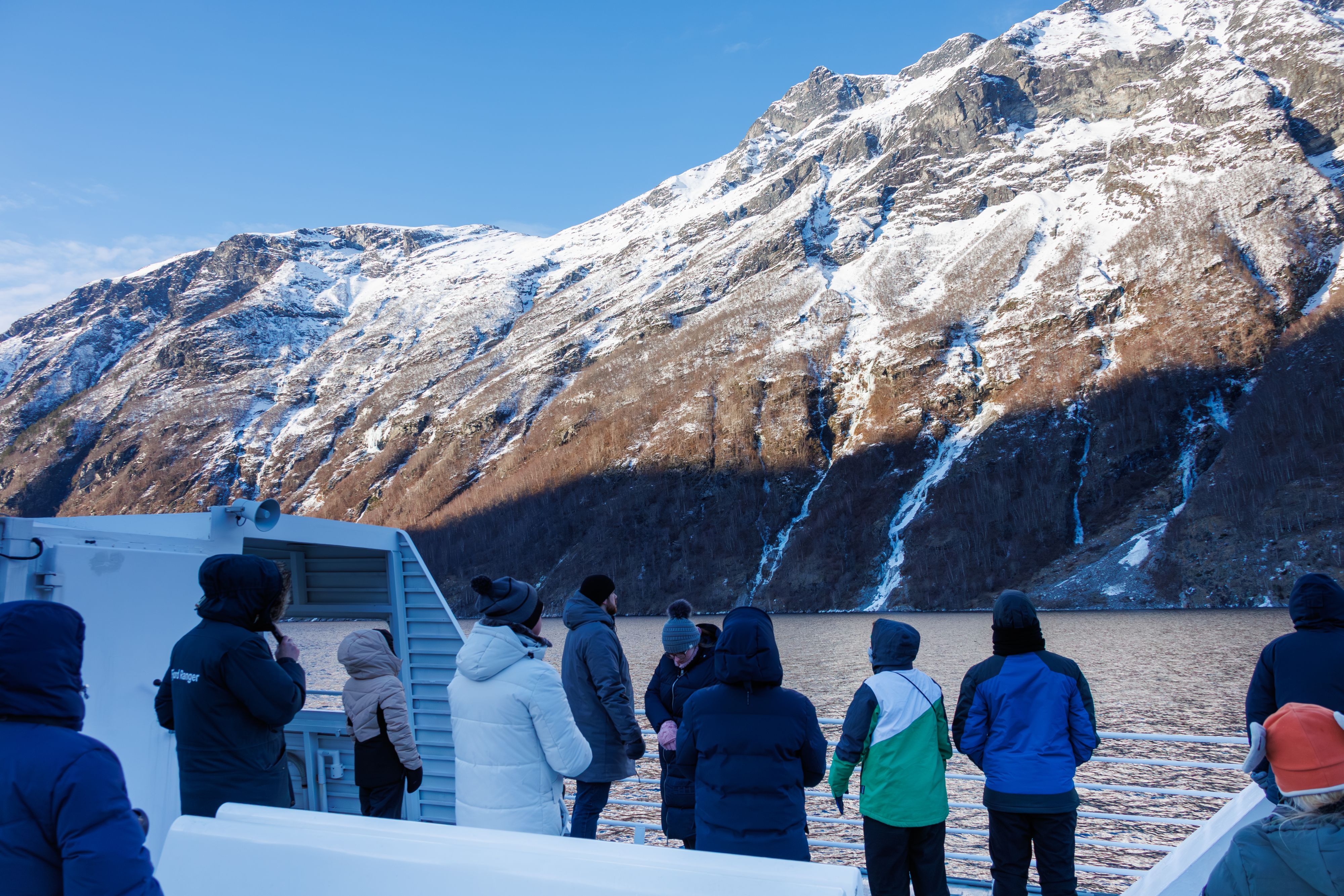 Passengers on a fjord cruise deck watching snow-covered mountains in Geiranger during winter, Norway