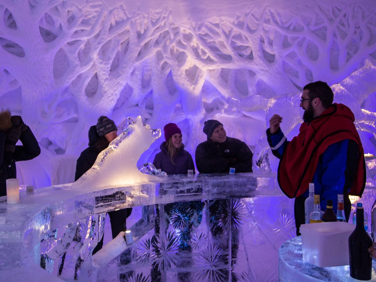 Gjester som nyter drinker i en isbar omgitt av opplyste snø- og isskulpturer på Snøresortet i Kirkenes.