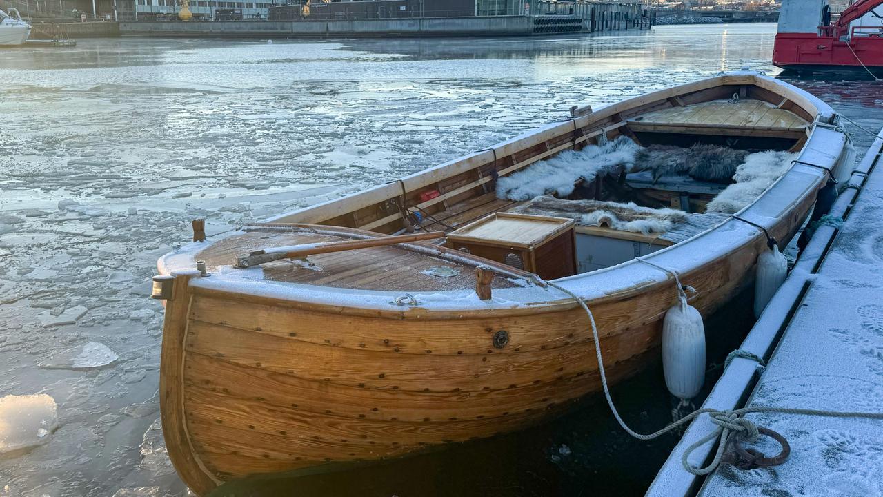 Traditionelles Holzboot mit Rentierfellen, vertäut in einem eisigen Hafen im Winter, Trondheim, Norwegen