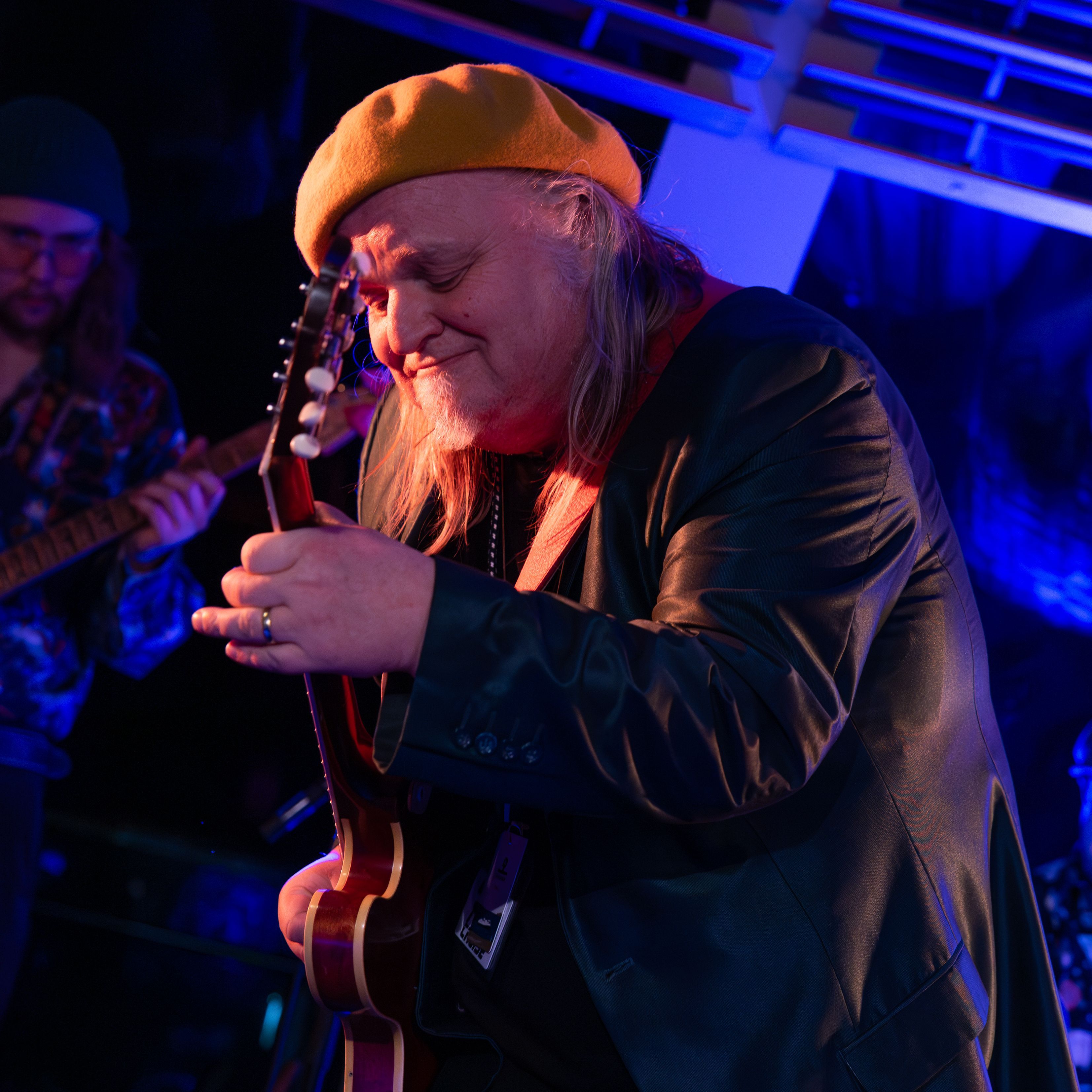 Knut Reiersrud fremfører et intimt live gitarsett om bord på Havila Voyages Blues Cruise 2027, opplyst av fargerikt scenelys.