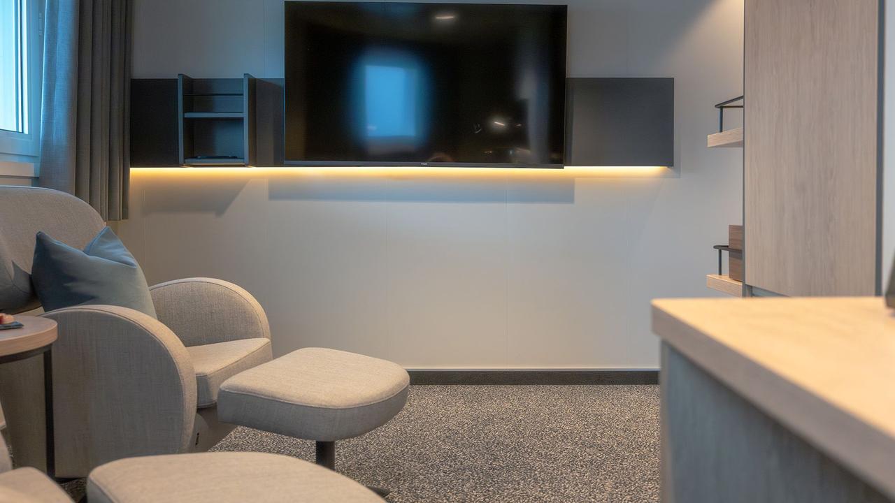 Loungebereich in der Aft View Mini Suite mit bequemen Sesseln, einem großen Flachbildfernseher, Einbauregalen und einem großzügigen Grundriss zum Entspannen.