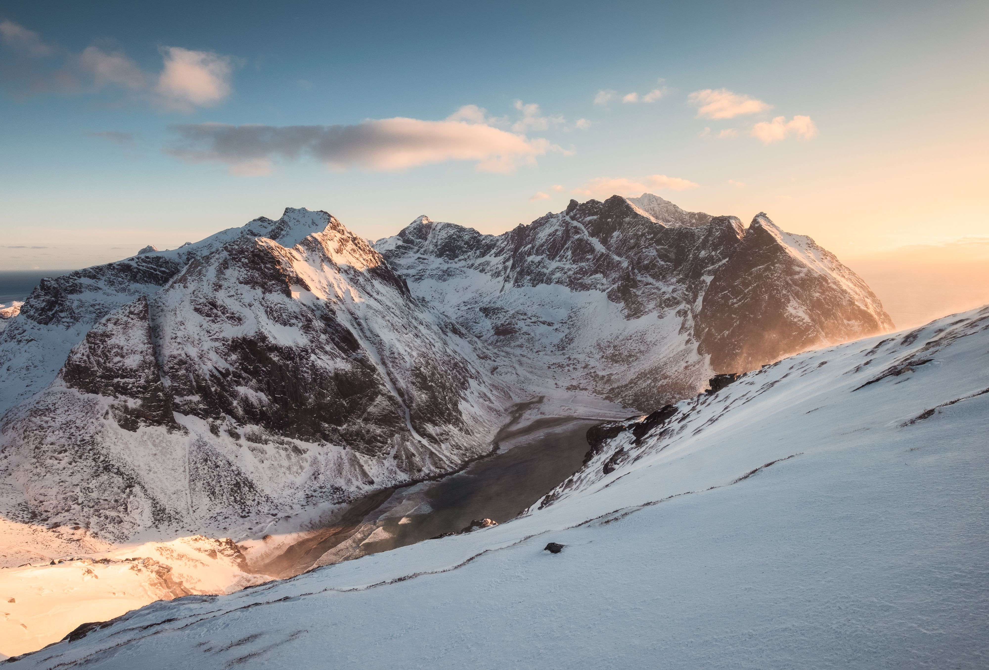 Schneebedeckte Berggipfel und ein zugefrorener Fjord, die im goldenen Februarlicht entlang Norwegens dramatischer arktischer Küste leuchten