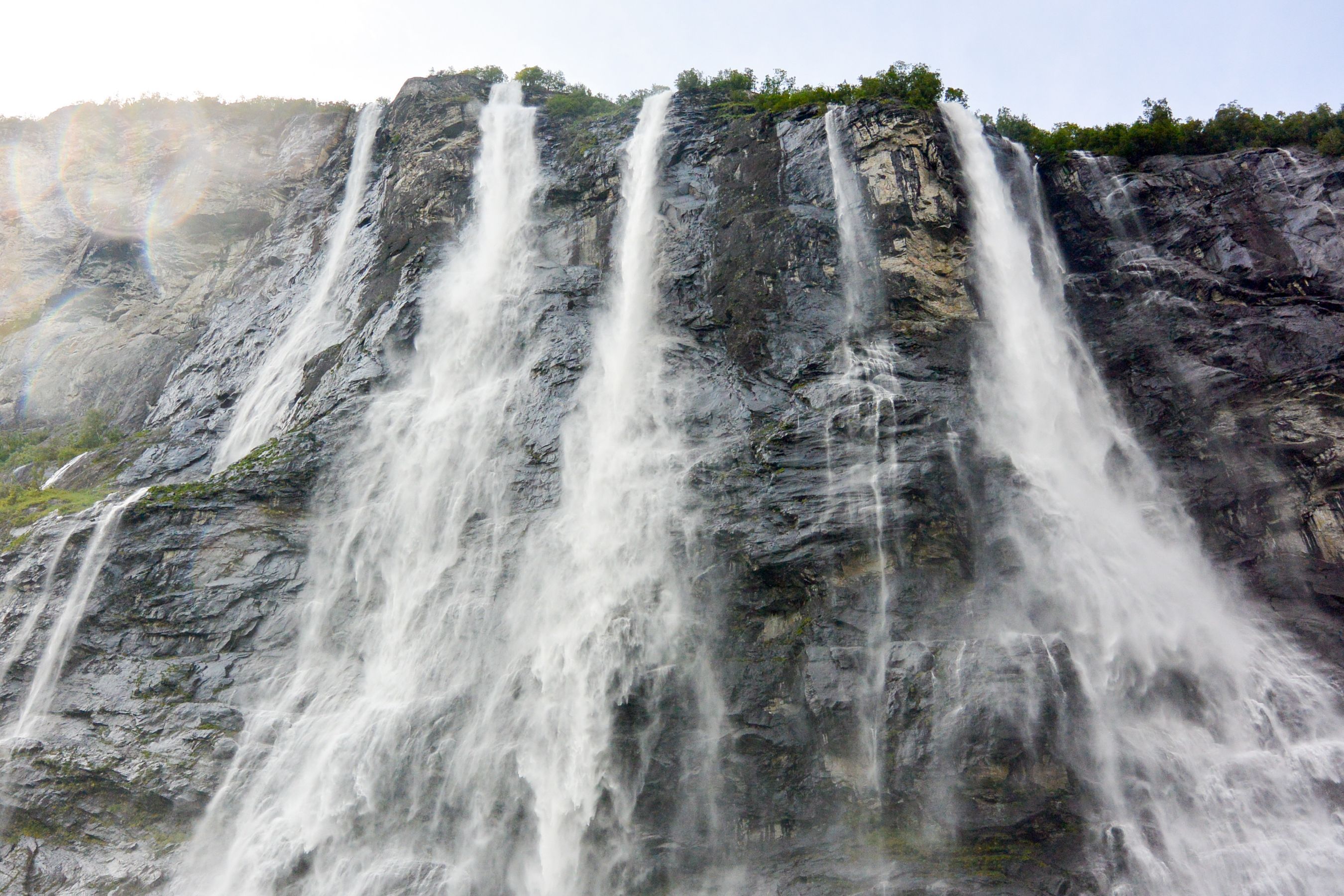 Vattenfallet De sju systrarna störtar nerför en brant klippvägg i Geirangerfjorden i Norge, där flera vattenströmmar faller dramatiskt ner i fjorden nedanför.