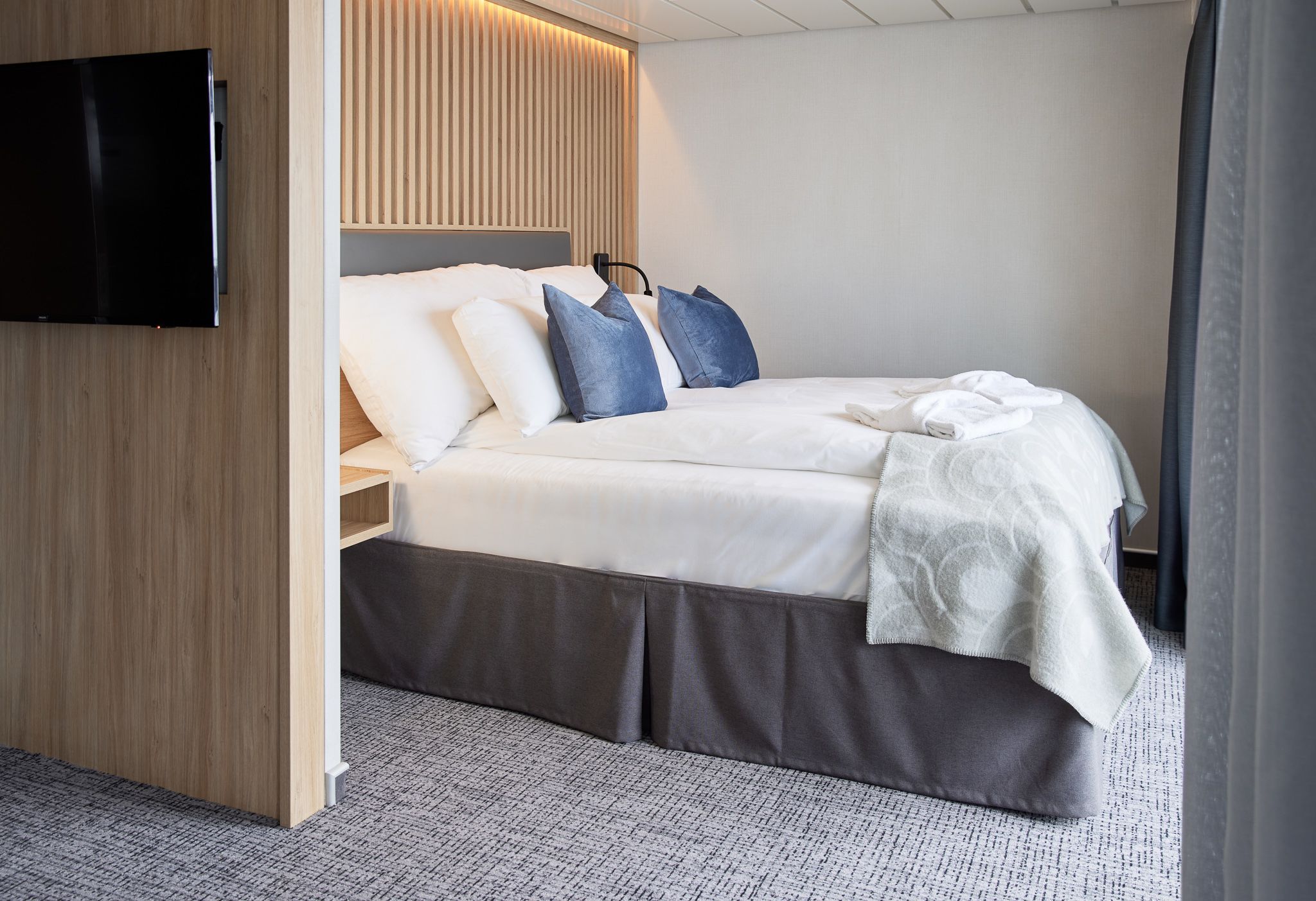 Tilgjengelig juniorsuite med dobbeltseng, myk belysning, moderne treverk og direkte tilgang til privat balkong med havutsikt.