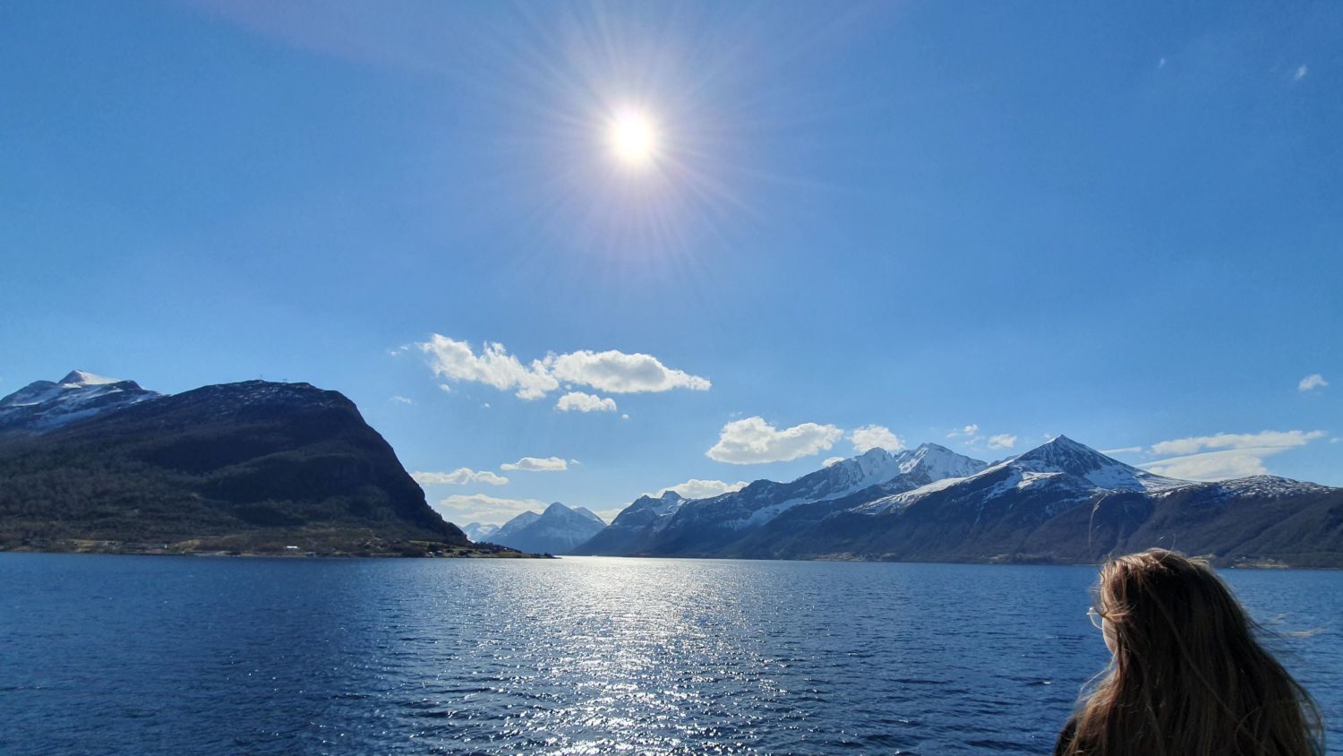 Reisender, der einen sonnigen Tag am Hjørundfjord genießt, mit funkelnd blauem Wasser und schneebedeckten Bergen, die in Westnorwegen eine atemberaubende Fjordlandschaft bilden.