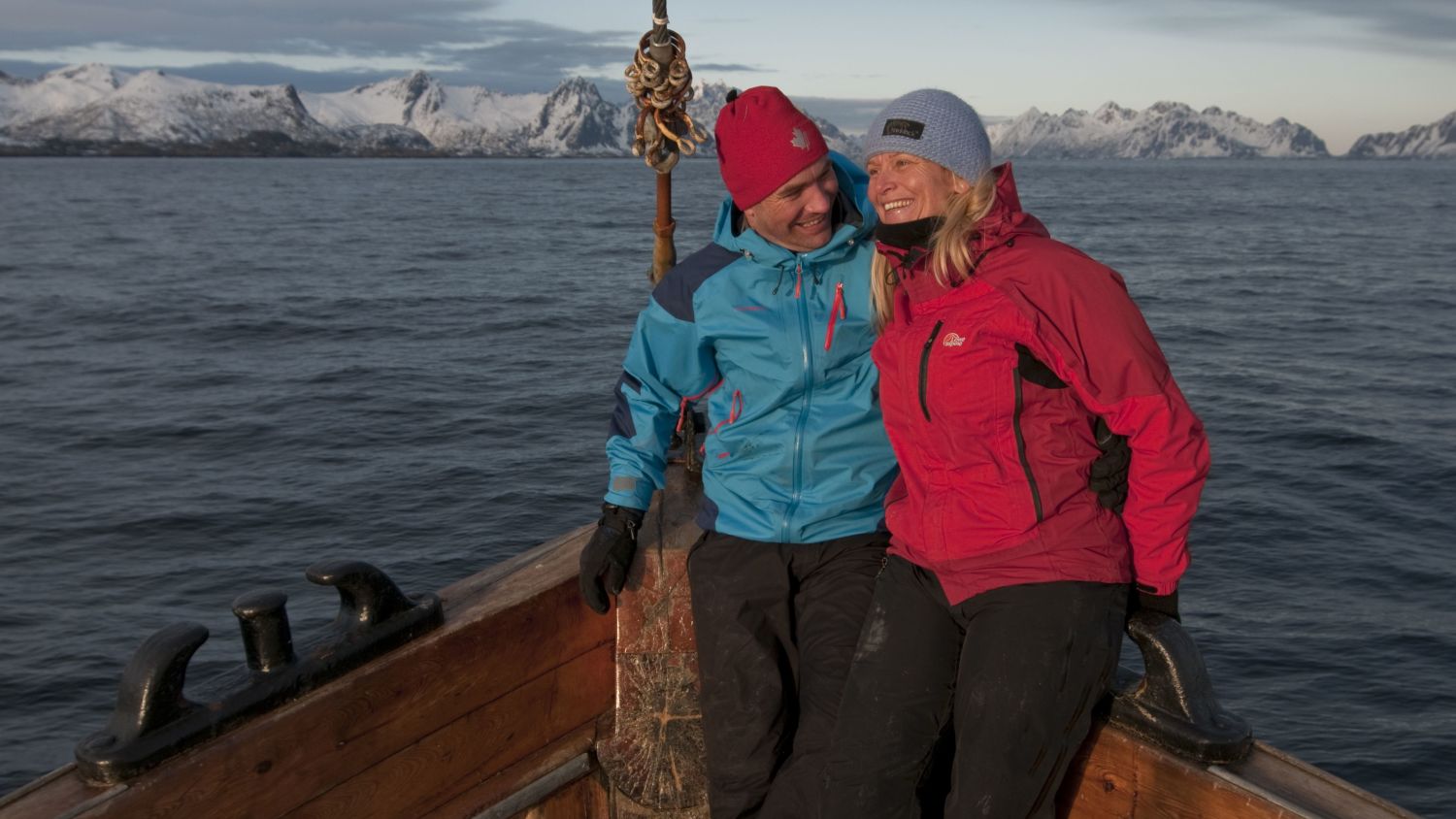 Paar genießt eine traditionelle Bootsfahrt auf dem Vestfjord mit den schneebedeckten Lofoten-Bergen im Hintergrund, Nordnorwegen.