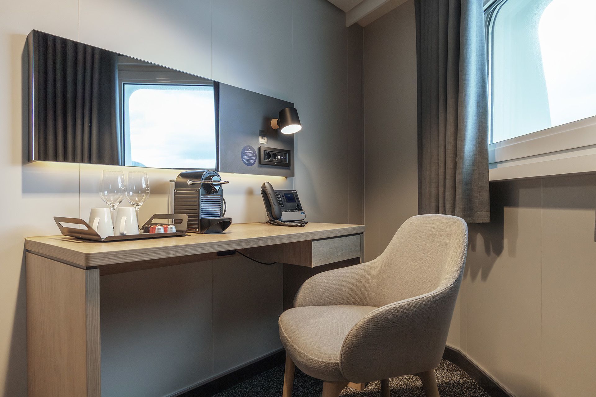 Arbeitsbereich in der Aft View Mini Suite mit Schreibtisch, Kaffeemaschine, Telefon, bequemen Stuhl und Fenster – ein praktischer Ort zum Entspannen oder zur Planung des Tages.