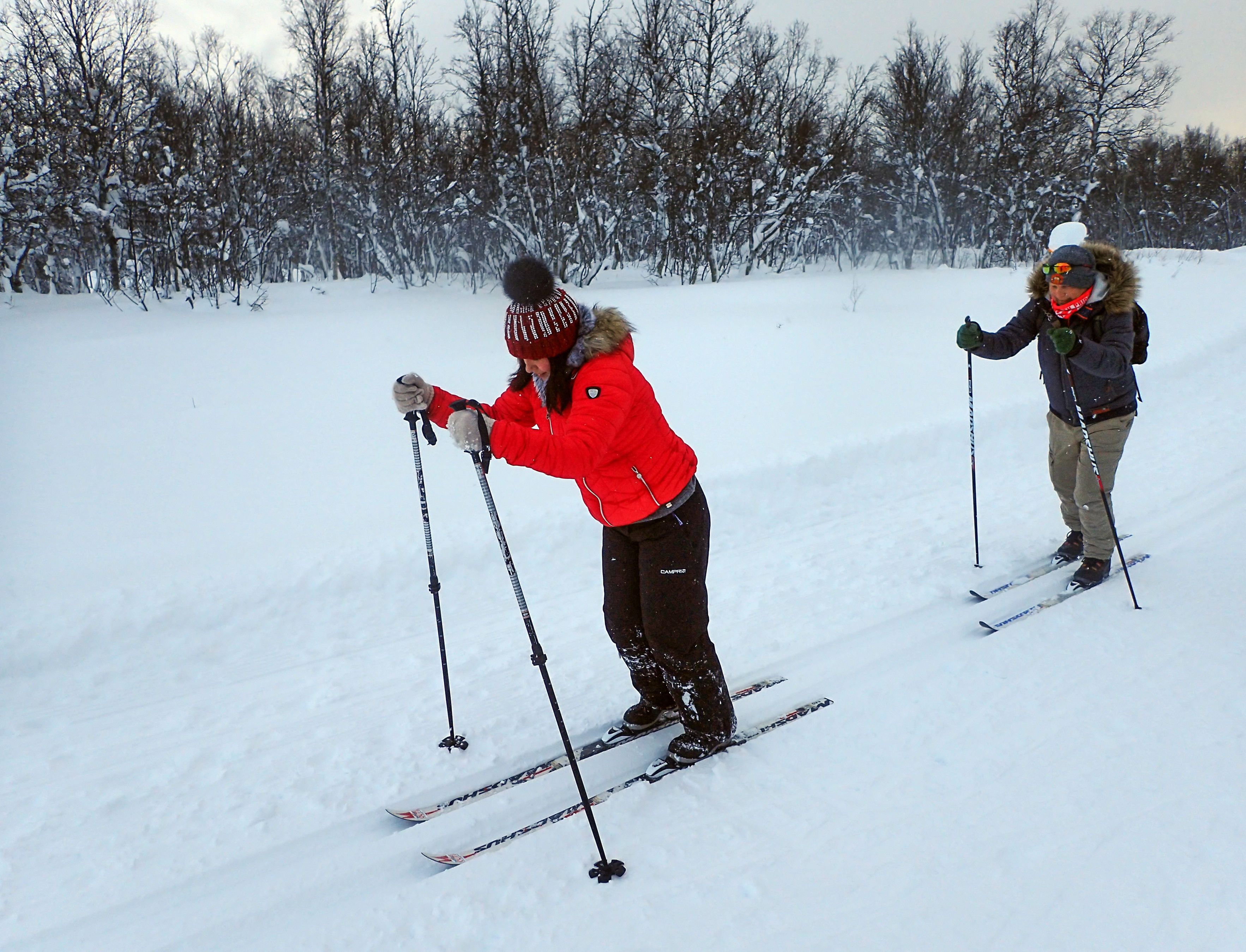To gjester som trener klassisk langrenn i preparerte løyper nær Tromsø under en nybegynnertime, omgitt av urørt snø og fredelig arktisk skog.