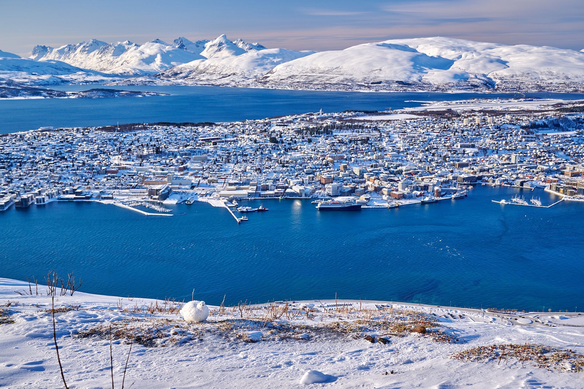Panoramautsikt over Tromsø om vinteren fra utsiktspunktet Fjellheisen, med snødekte fjell, arktiske fjorder og byens havneområde nedenfor.