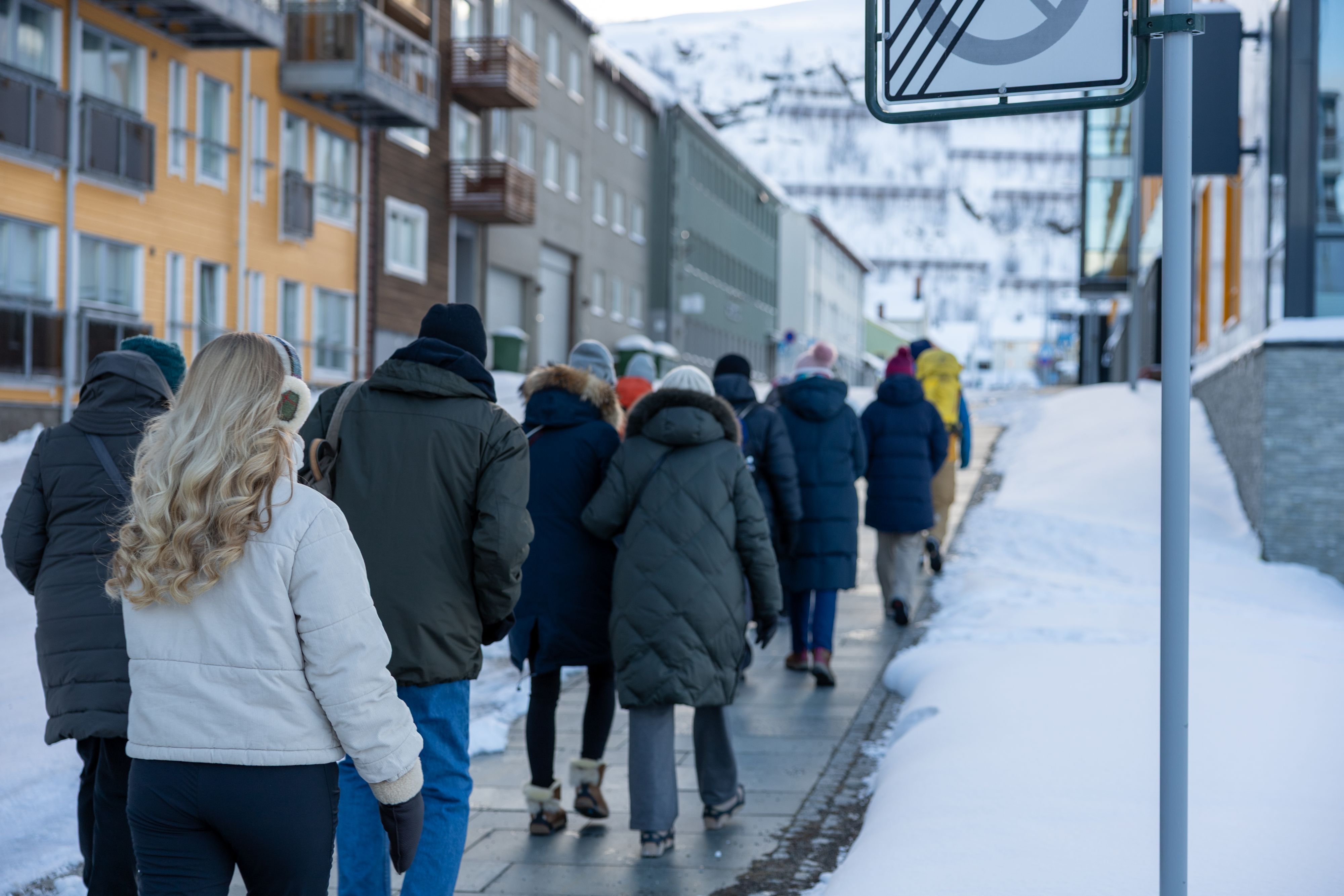 Gruppe med varmt kledde besøkende som går langs en snødekt gate på en guidet byvandring i Hammerfest, Norge