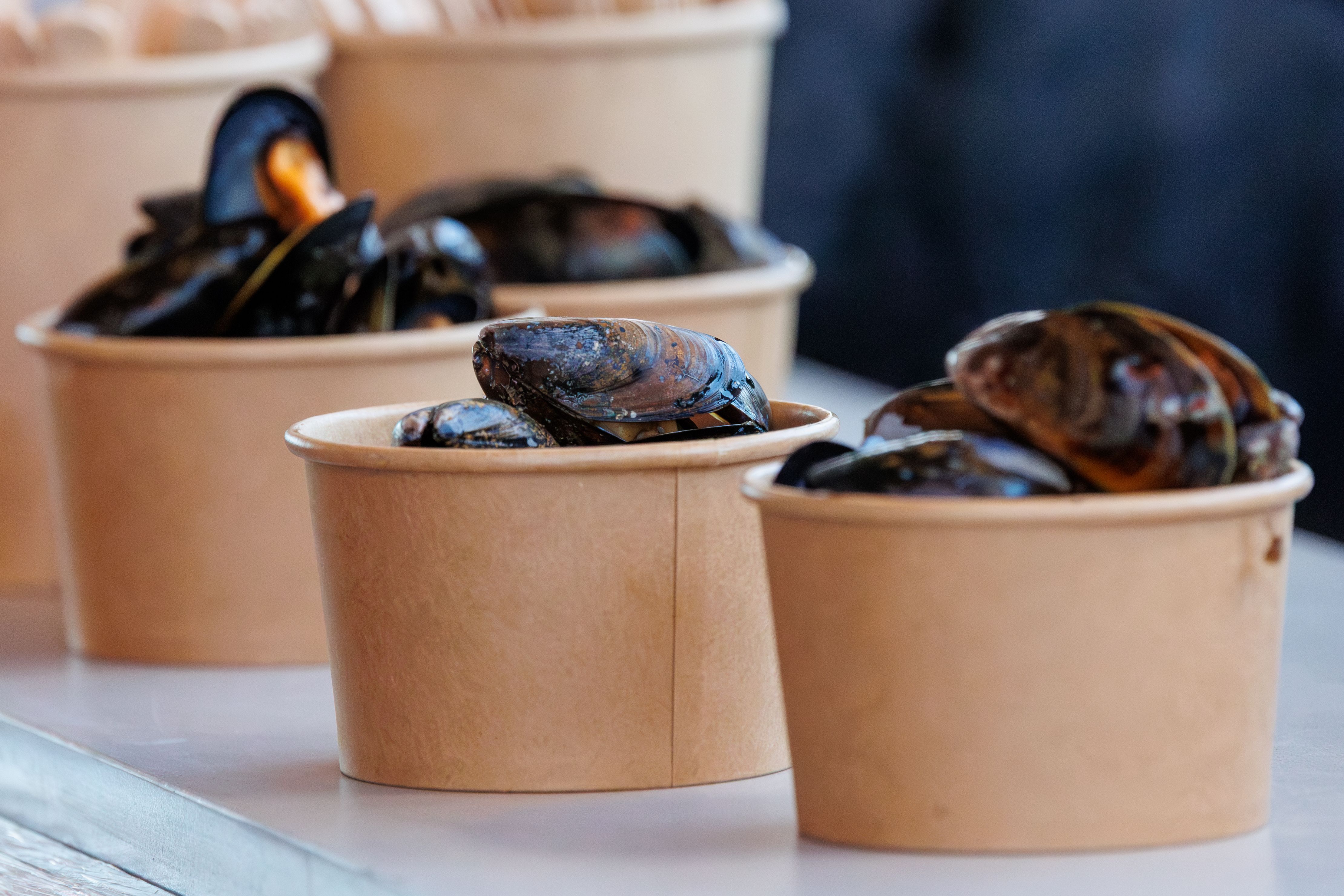 Steamed mussels served in paper cups for a tasting on board