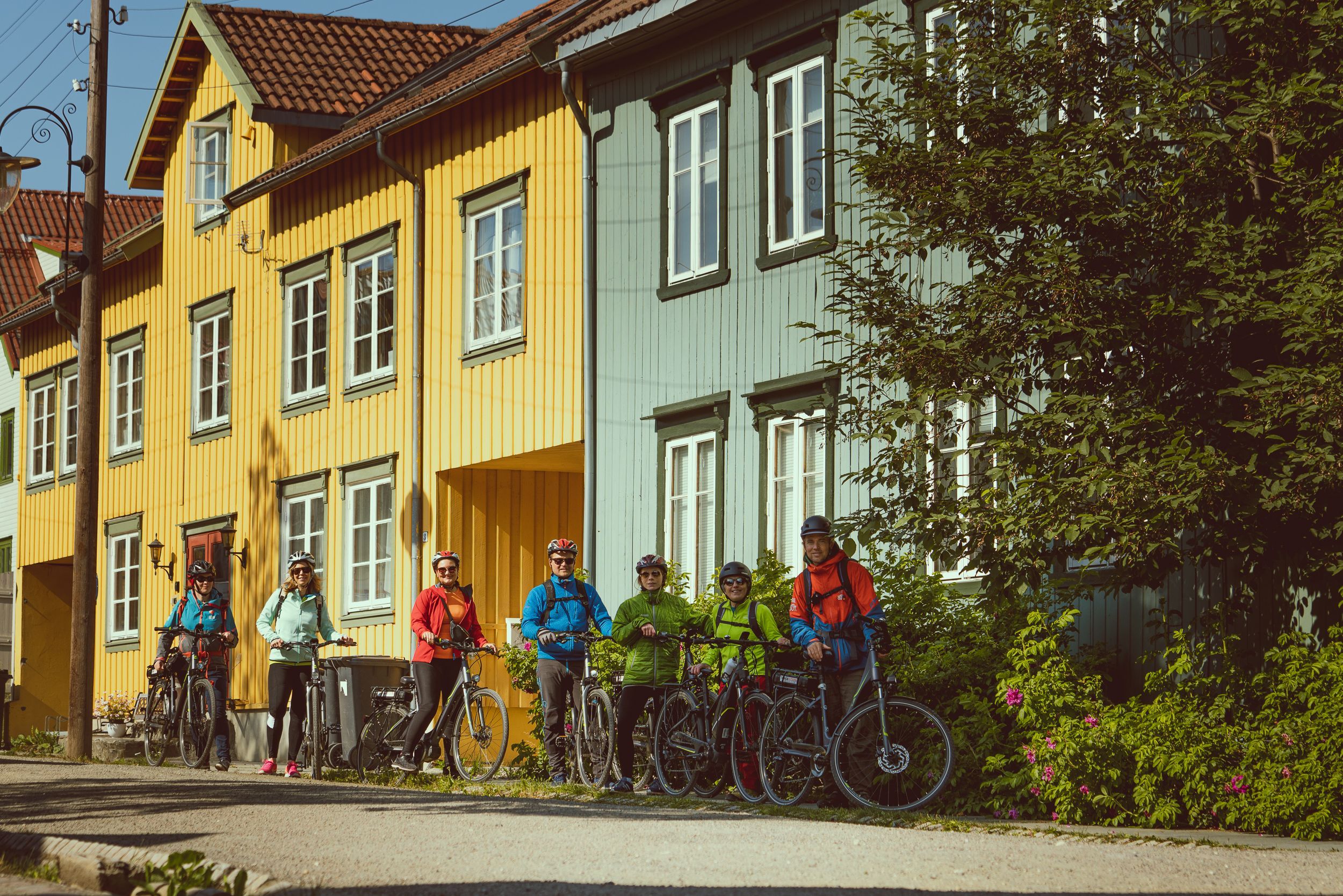 Gruppe syklister på en guidet elsykkeltur gjennom Tromsøs historiske nabolag med fargerike trehus.