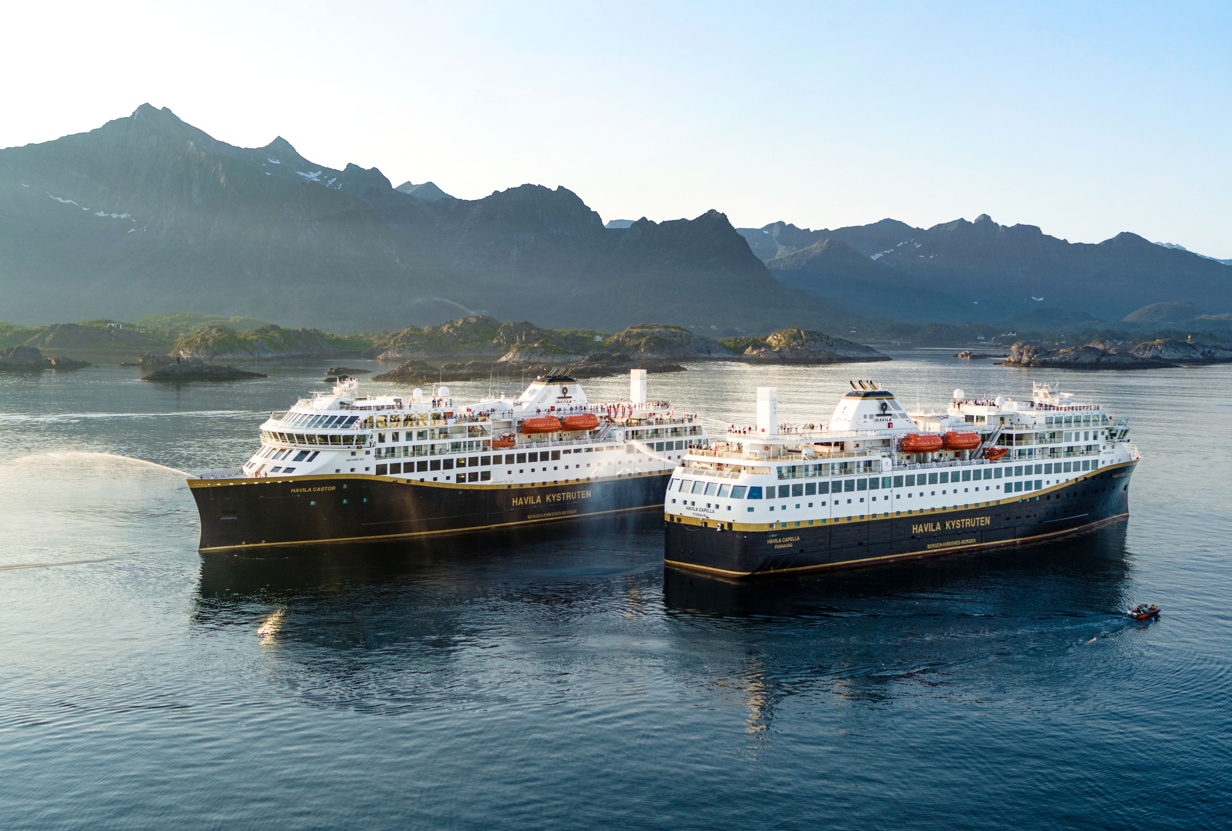Two Havila Voyages ships sailing together along the Norwegian coast.