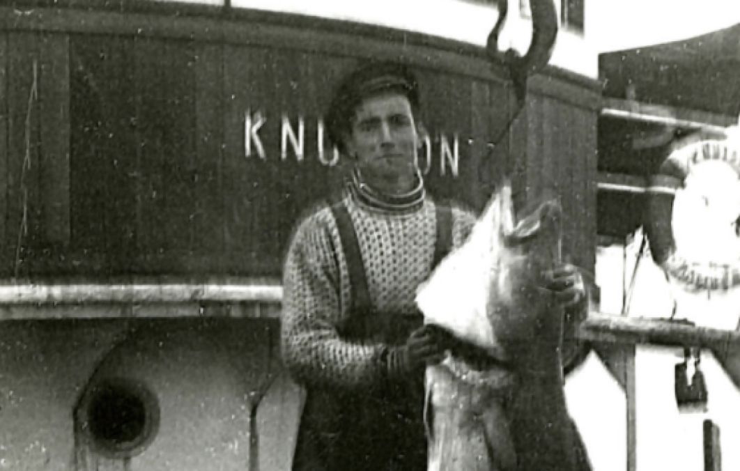 Young Per Sævik holding a large cod beside a fishing vessel in Norway.