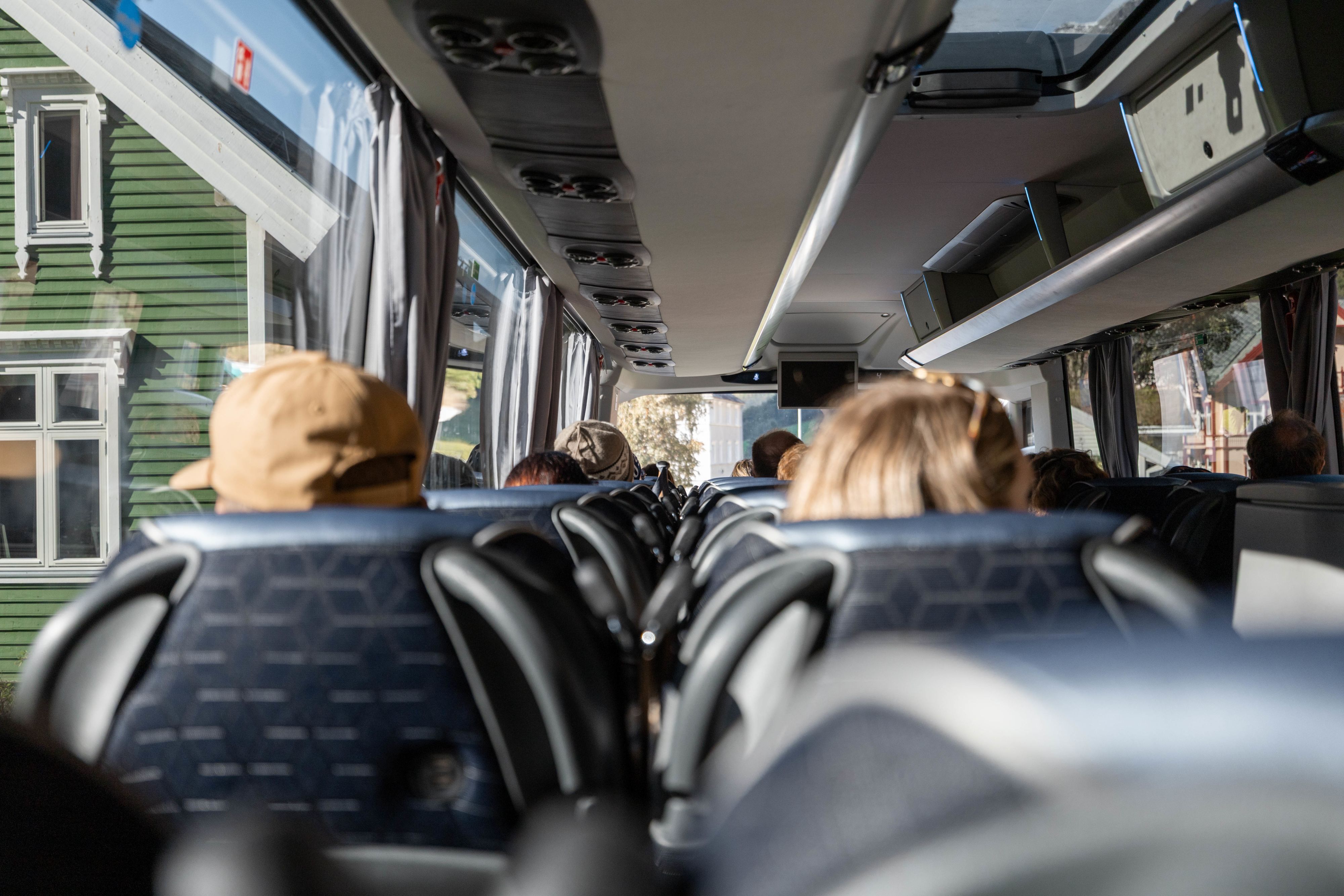 View from inside a tour bus with passengers passing a green wooden house on a sightseeing trip in Norway
