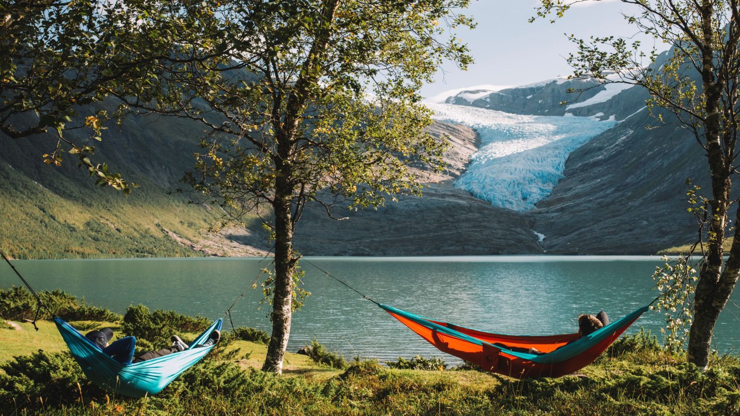 Menschen, die in Hängematten an einem Gletschersee entspannen, mit einem beeindruckenden norwegischen Gletscher und Bergen im Hintergrund