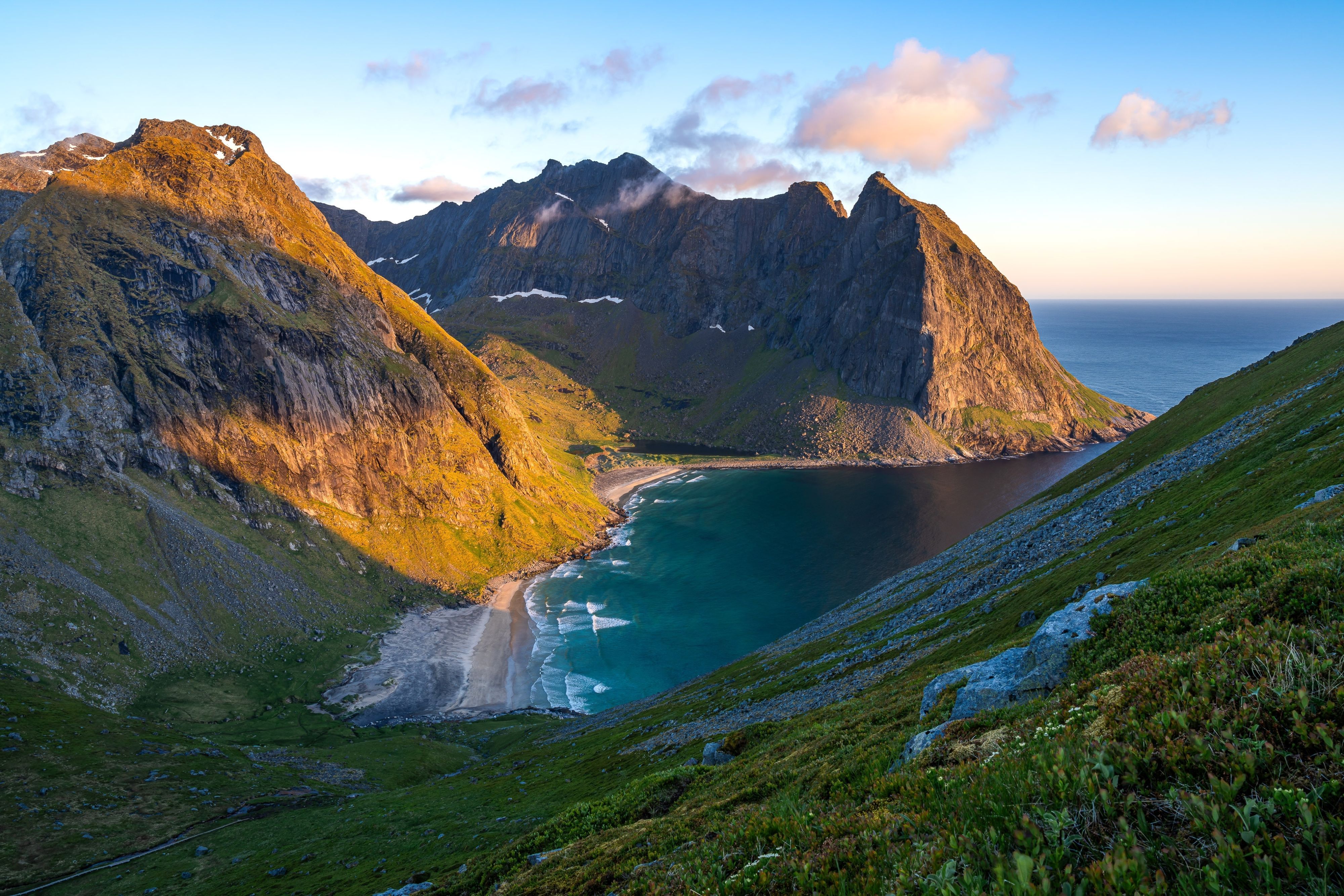 Utsikt over Kvalvika-stranden i Lofoten under midnattssolen, med turkis vann, dramatiske fjell og gyllent junilys langs Norges kyst