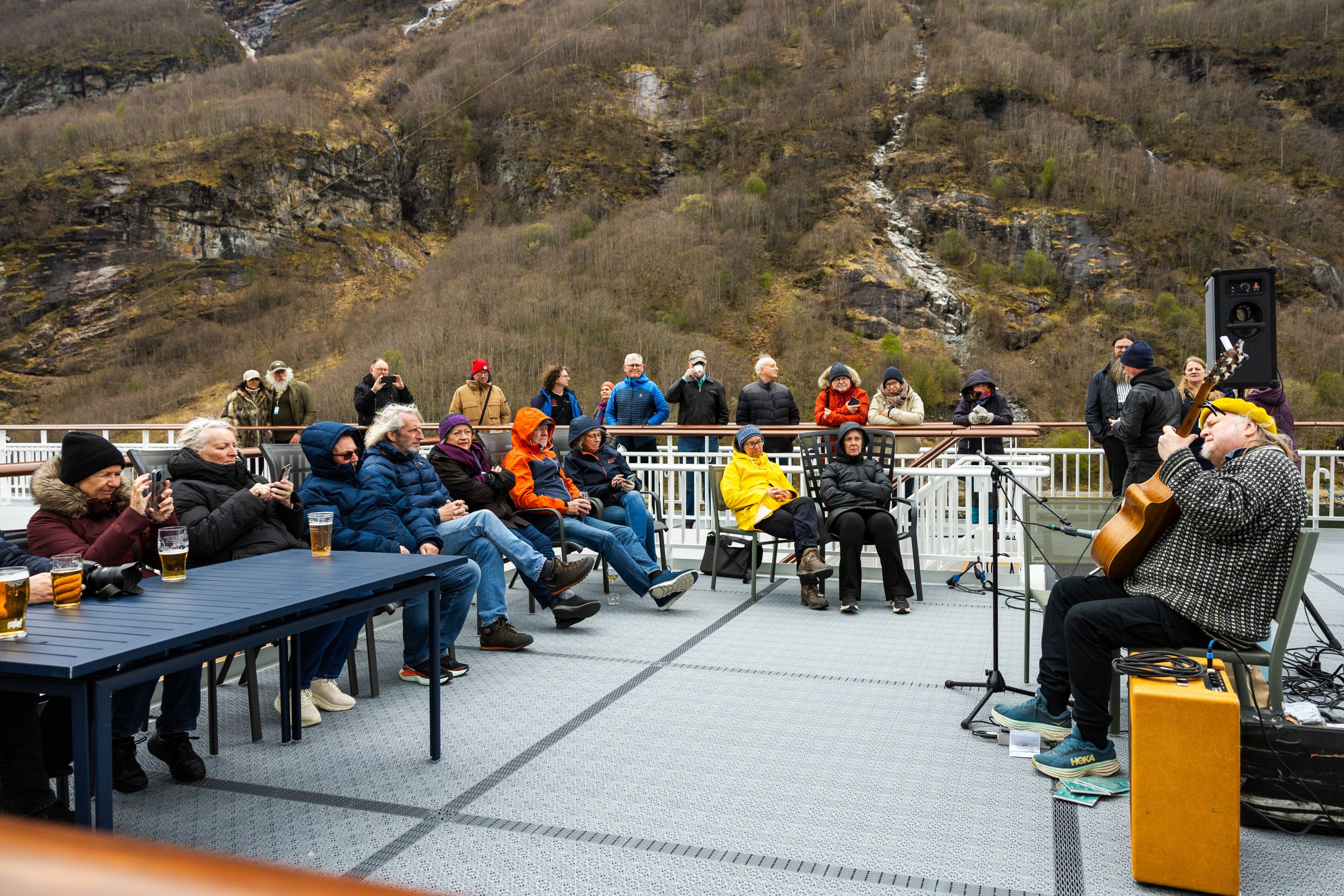 Knut Reiersrud holder en live utendørskonsert på dekk under Havila Voyages Blues Cruise 2027, mens gjestene nyter musikken med Norges dramatiske fjordlandskap som bakteppe.