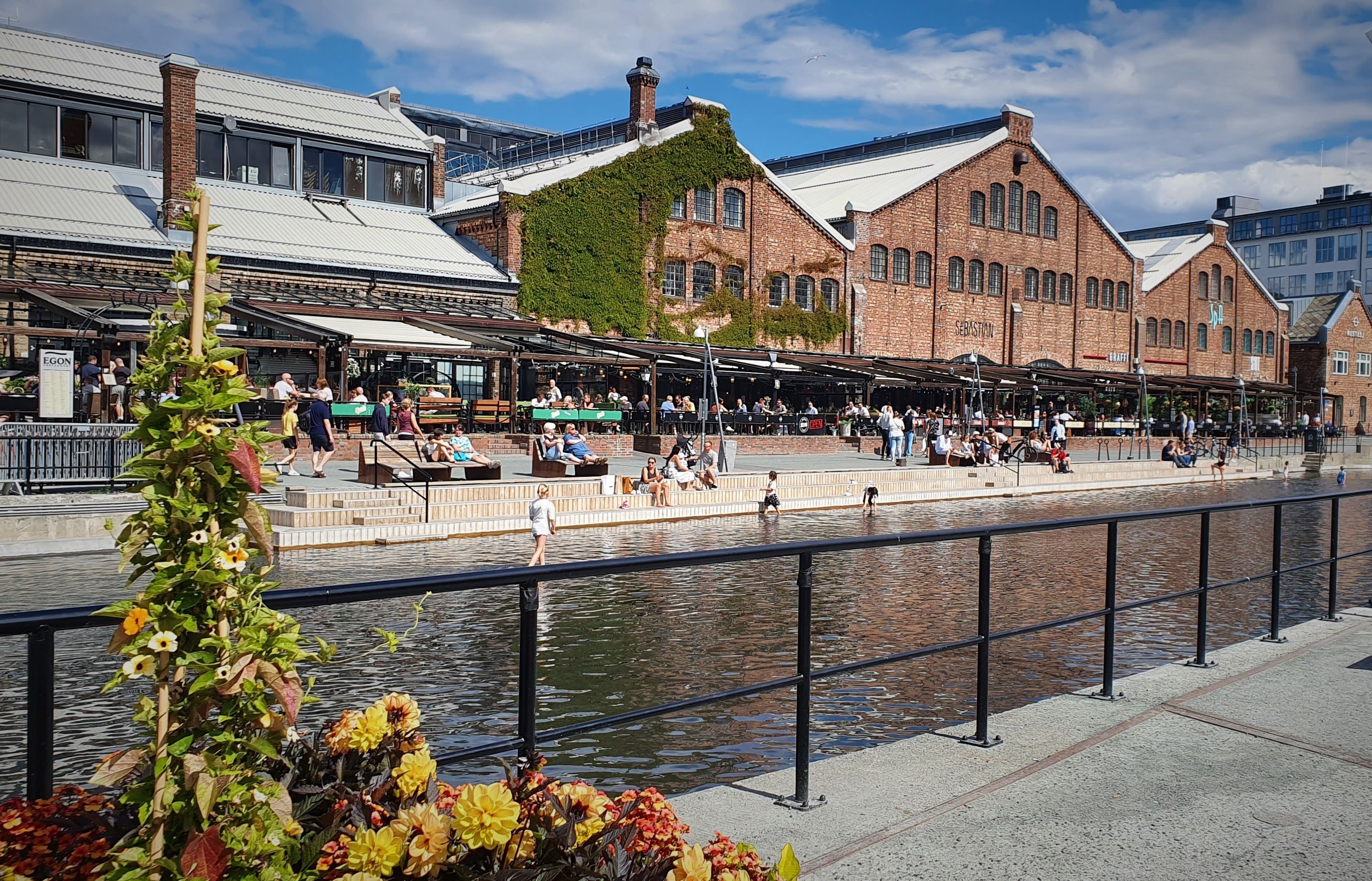 Folk som slapper av ved vannet på Solsiden, med restauranter og gamle mursteinslagerbygninger i Trondheim, Norge