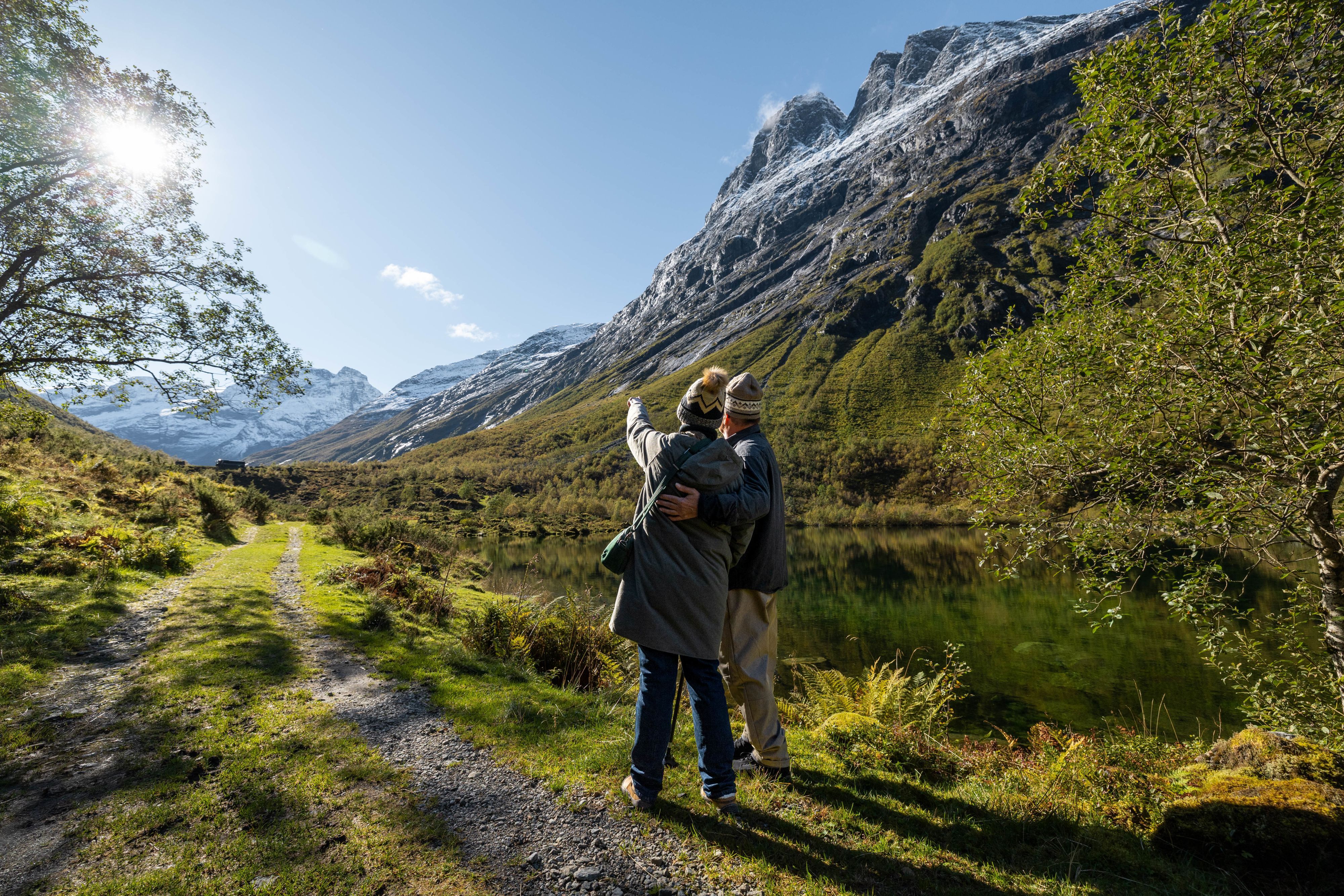 Couple admiring snow-capped mountains by a calm lake on a hiking trail in rural Norway