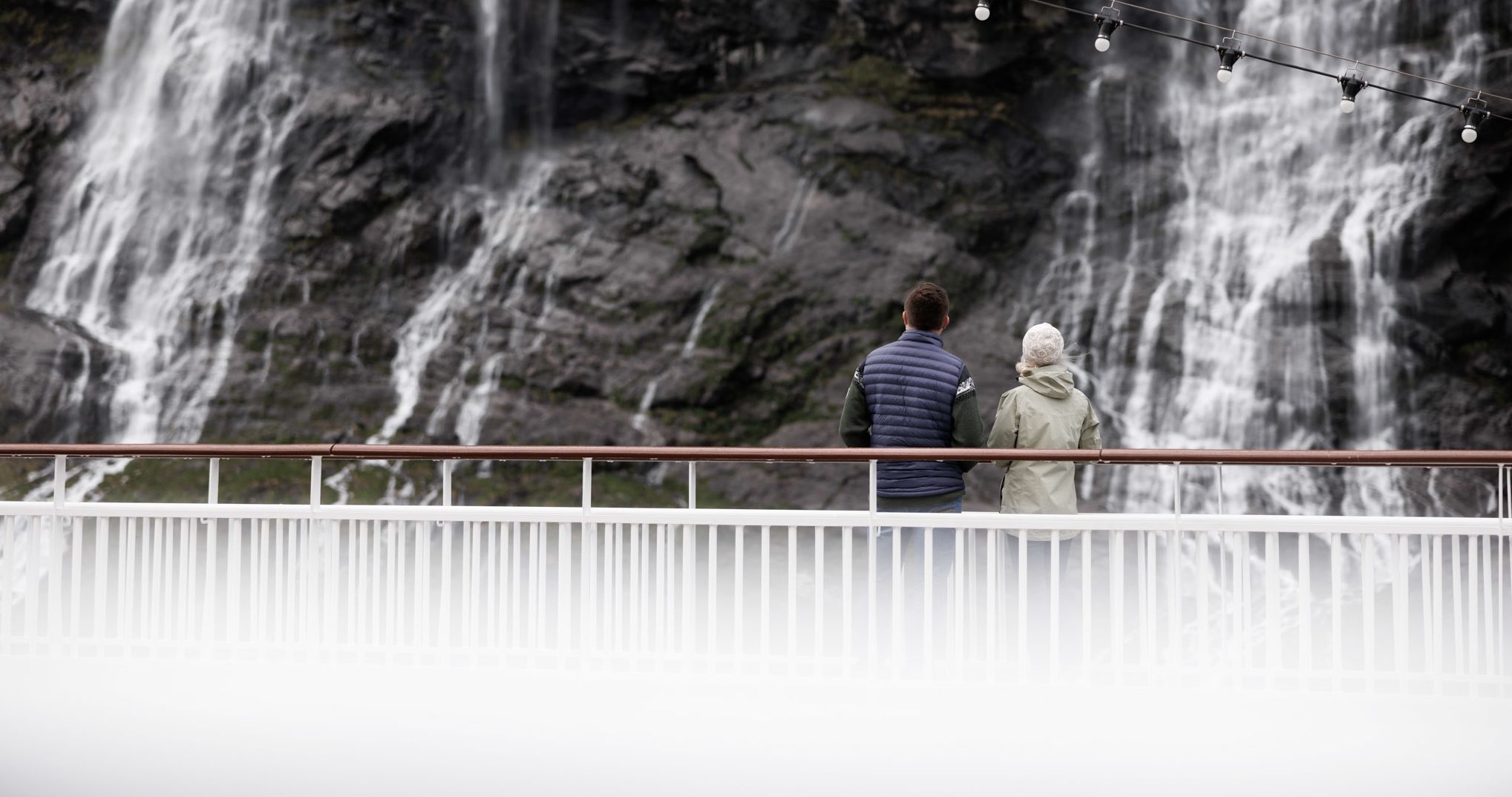 Par ved skipsrekkverket som ser fossefallene styrte nedover klippene i Geirangerfjorden