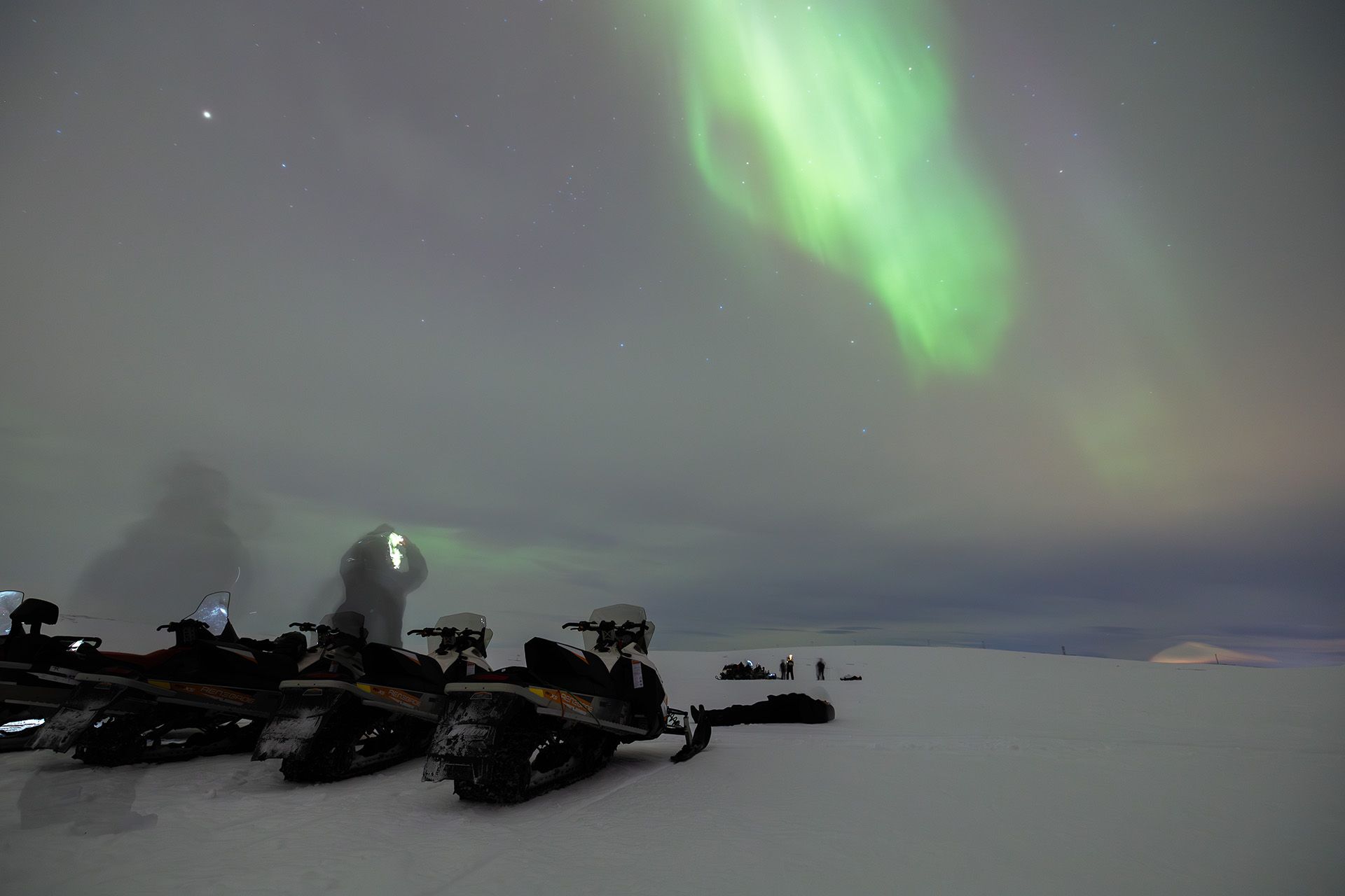 Tourist taking photo of northern lights next to two snow mobiles