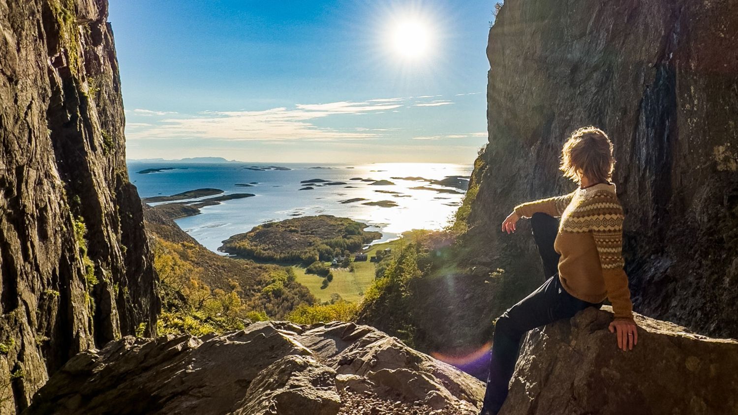 Hiker resting between steep cliffs overlooking islands and the Norwegian coast.