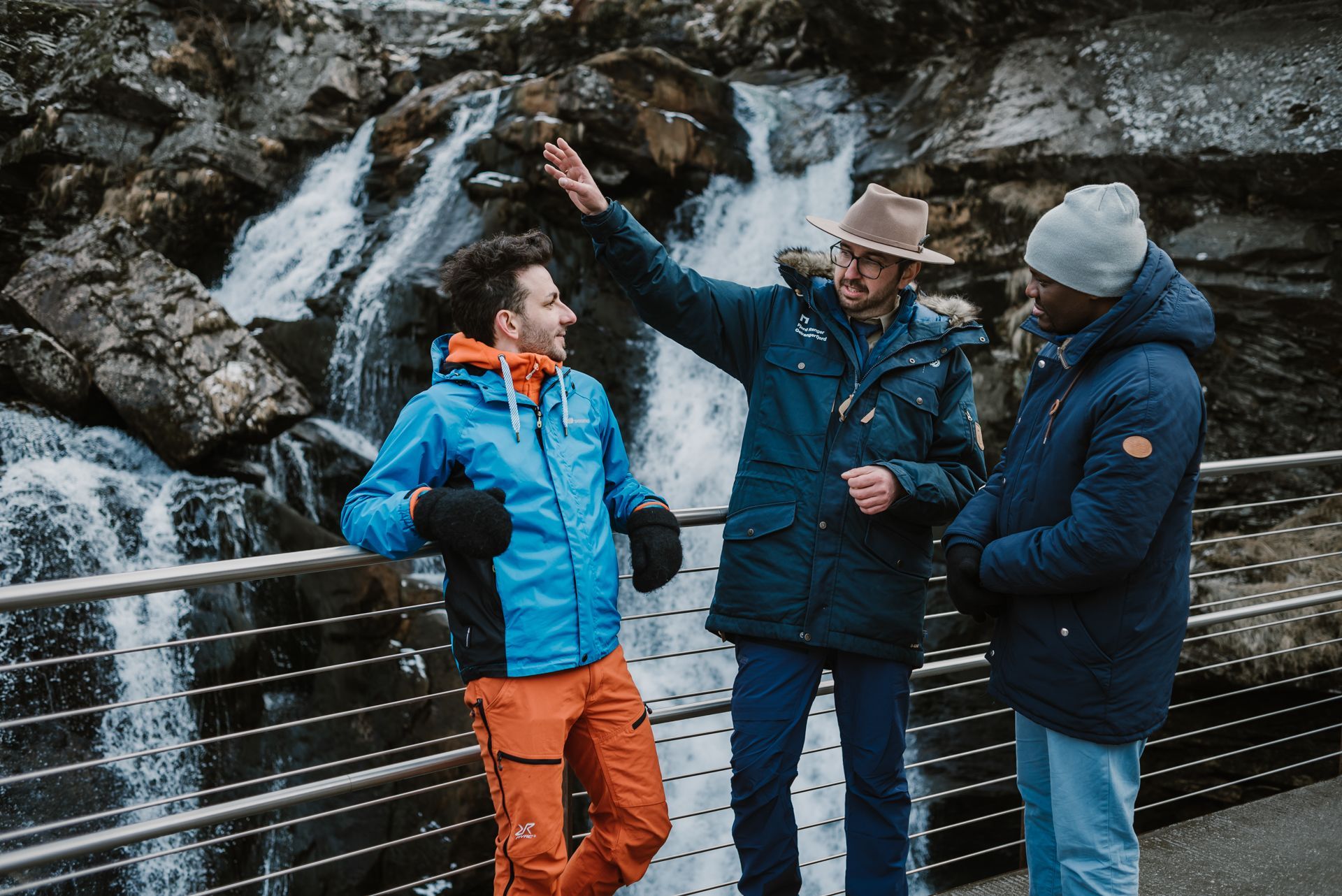 Fjord Ranger-guide som peker ut en foss for to turister i Geiranger under en vintertur, Norge