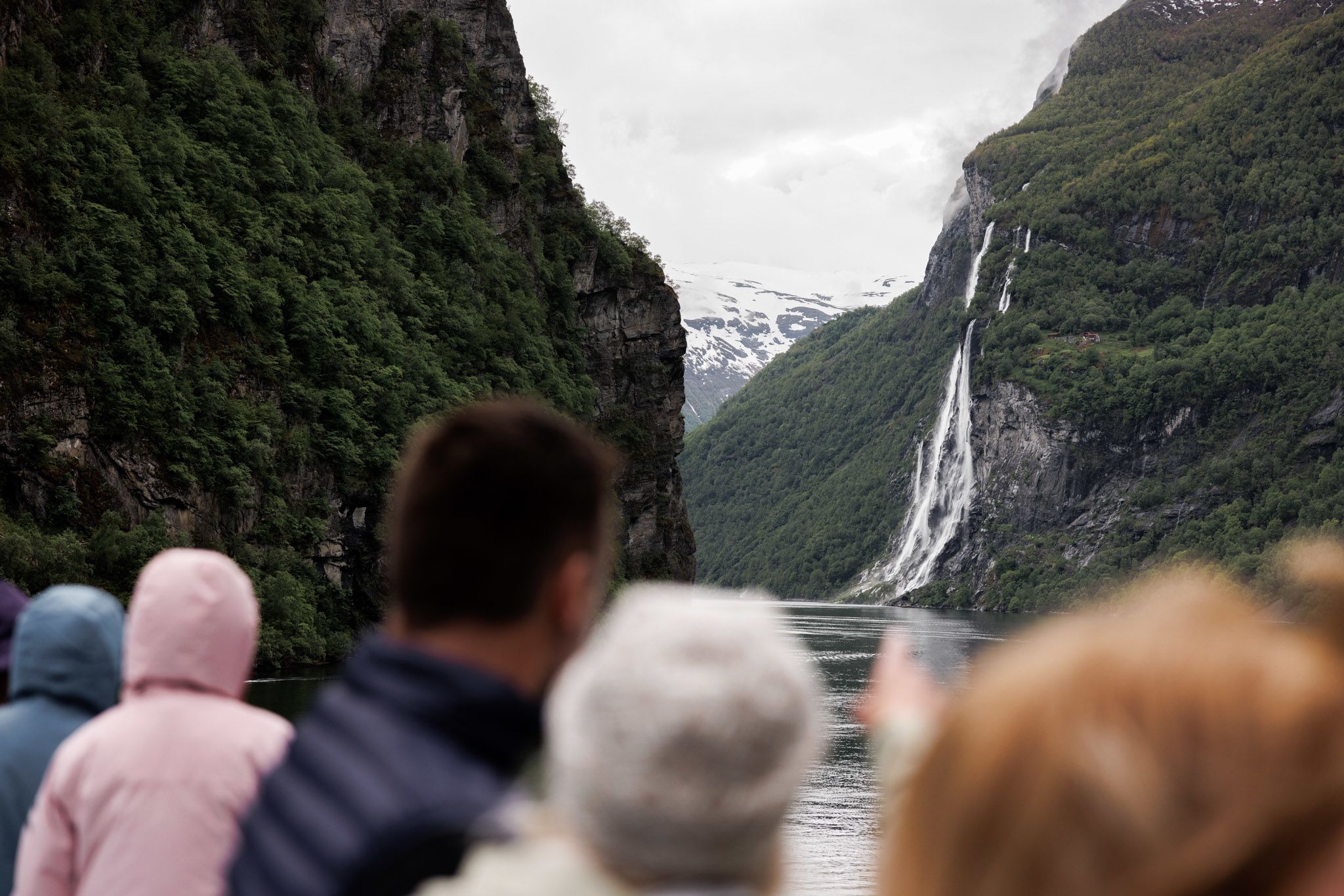 Kryssningsgäster beundrar vattenfallet De sju systrarna som störtar nerför klipporna i Geirangerfjorden, omgivet av branta berg och snötäckta toppar i Norge.