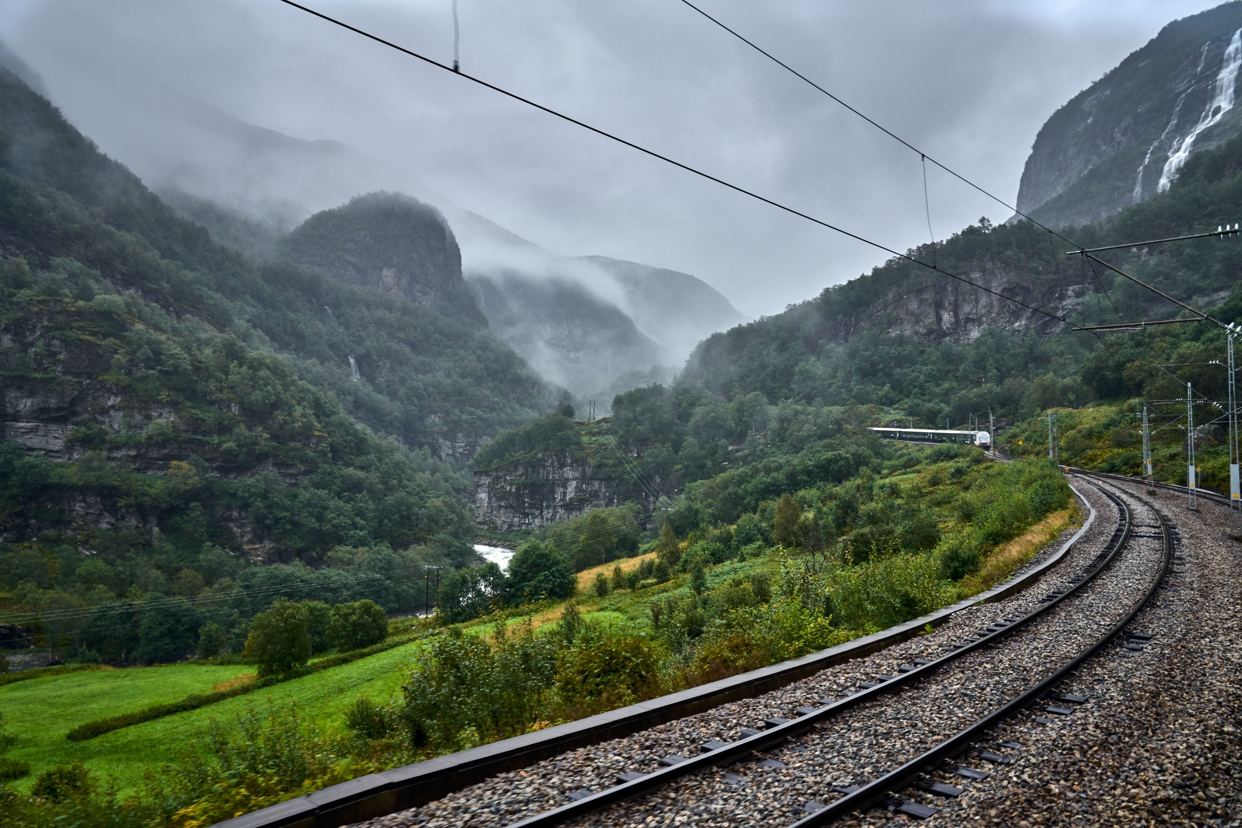 Flåmsbanan som slingrar sig genom dimhöljda berg, vattenfall och frodiga dalar i Norge.