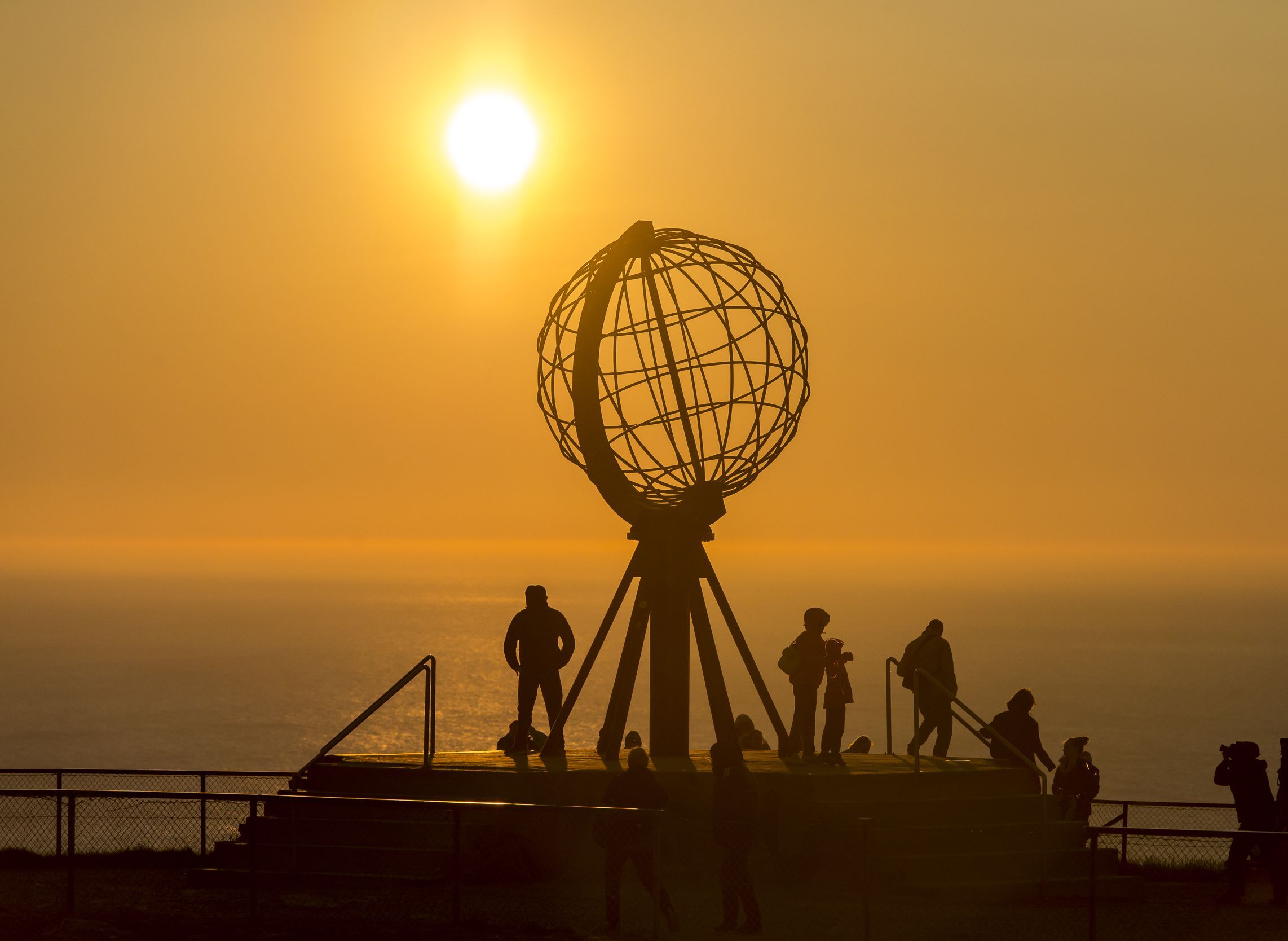 Besøkende som ser midnattssolen ved Nordkapp-globusen i Norge, med den gyldne solen som skinner over Polhavet