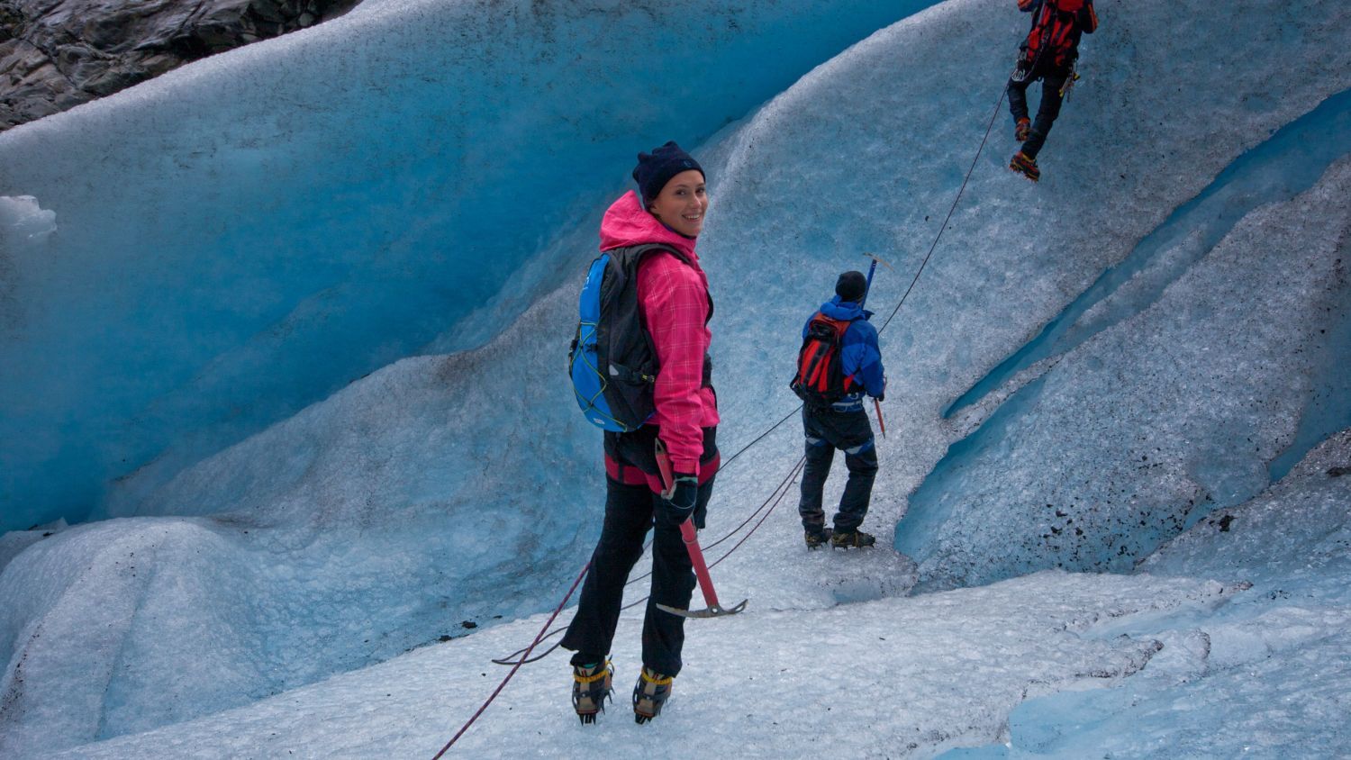 Geführtes Gletscherwanderabenteuer in Norwegen mit Bergsteigern, die mit Steigeisen und Seilen über blaues Gletschereis gehen