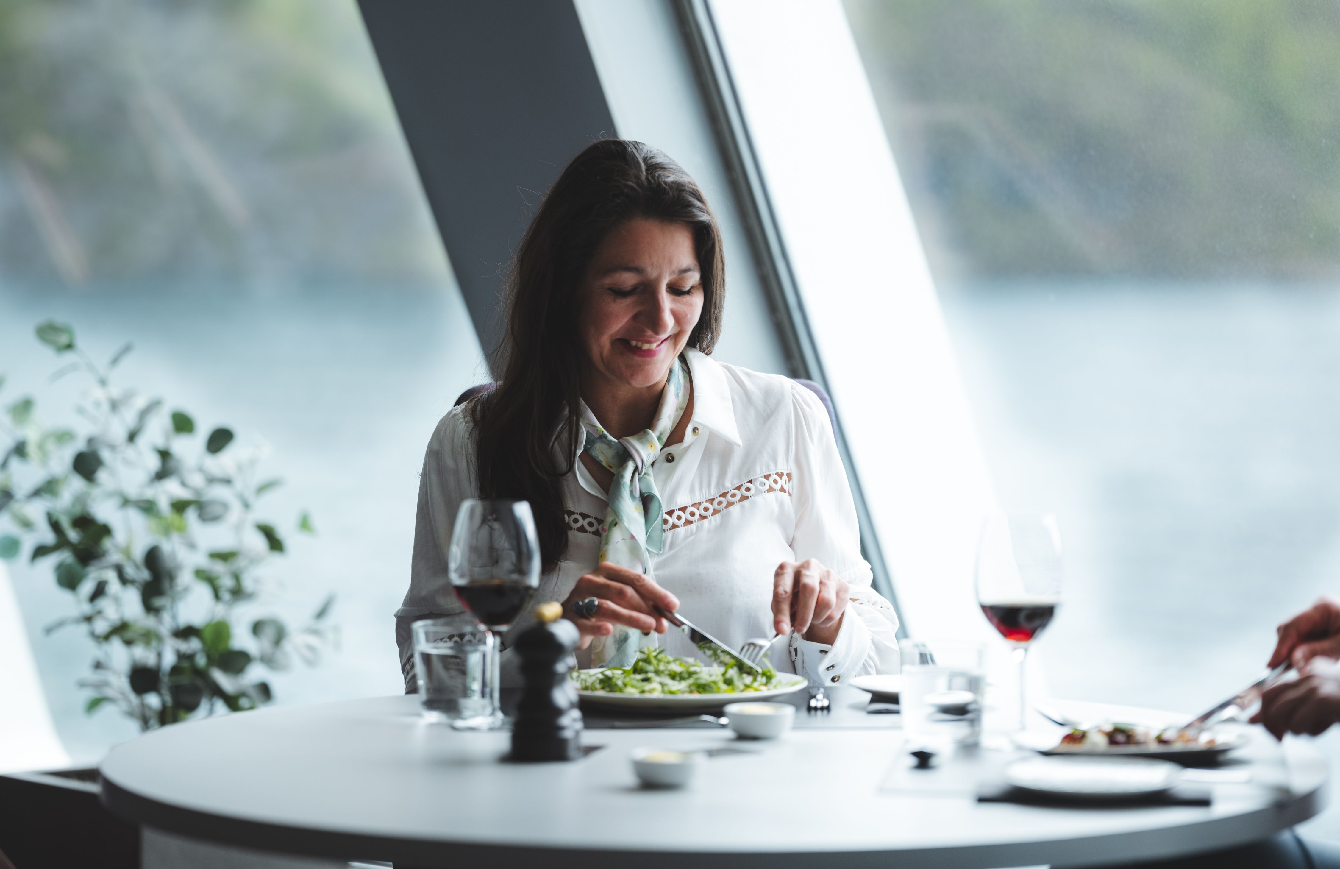 Gäst som avnjuter en måltid med ett glas rött vin vid ett fönsterbord med utsikt över fjorden