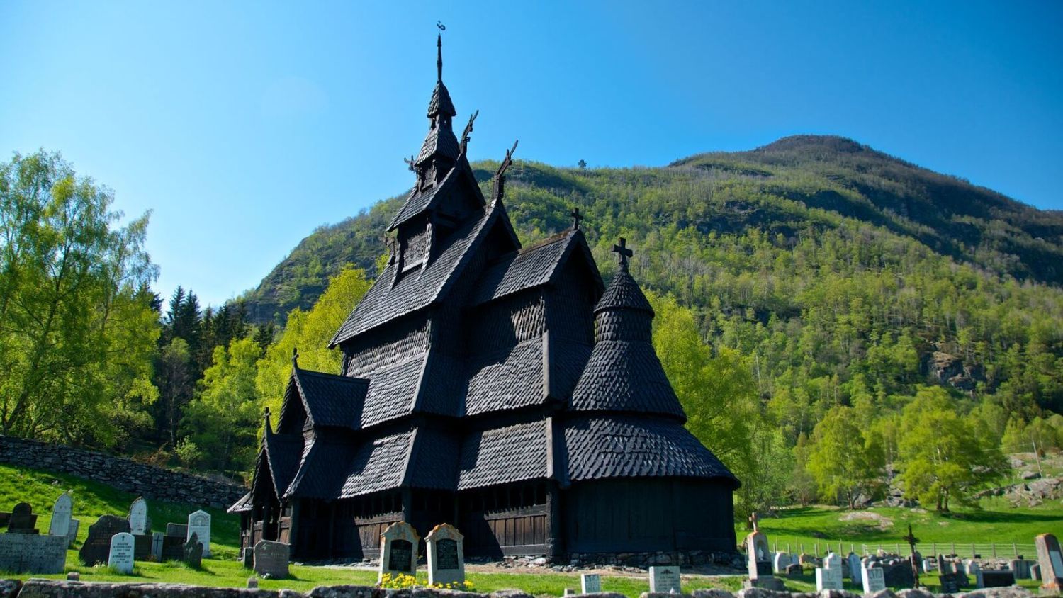 Traditionelle norwegische Stabkirche mit geschnitzten Drachenkopf-Dachverzierungen, steilen Holzschindeln und dramatischer Berglandschaft, die das Wikingererbe und die mittelalterliche Architektur widerspiegelt