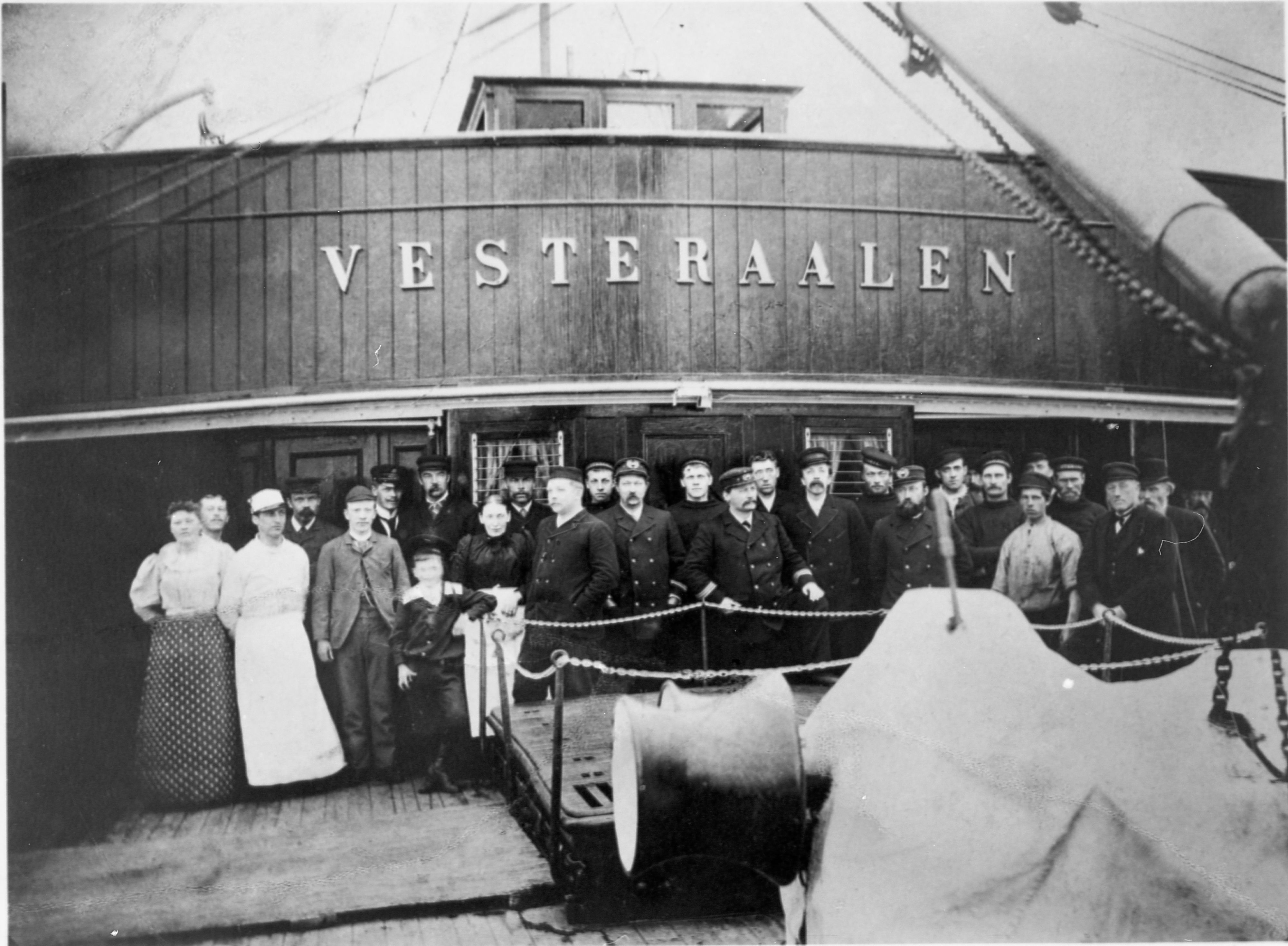 Historisk svart-hvitt gruppefotografi av mannskap og ansatte om bord på MS Vesterålen, et av de opprinnelige skipene i Hurtigruten, stående på dekk under skipets navn.